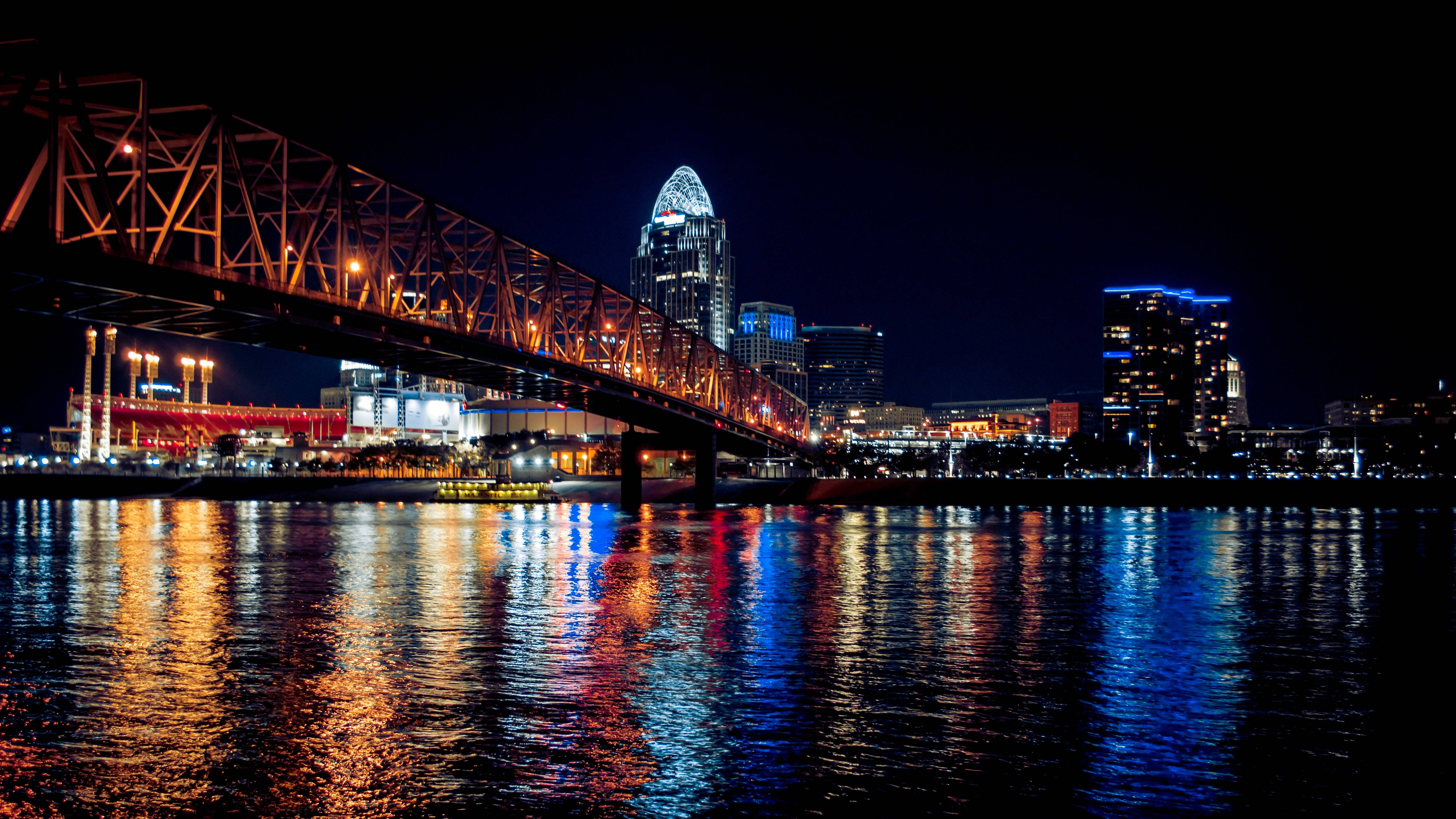 lights 桌布 壁紙 — 充滿活力的夜間城市景觀，一座亮燈的橋樑橫跨河流，反射摩天大樓的彩色燈光。