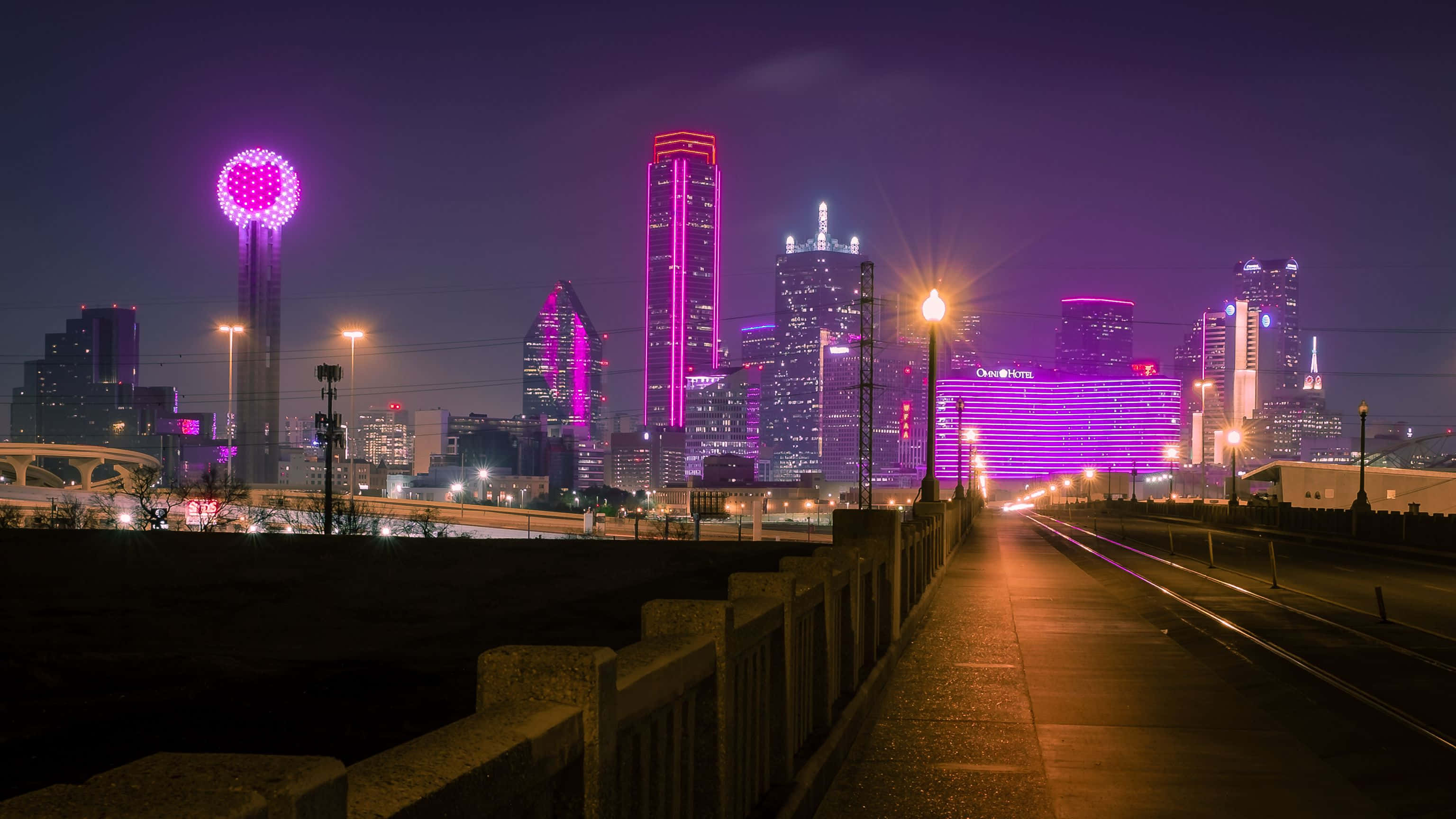 Light 桌布 壁紙 — 充滿活力的夜間城市景觀，摩天大樓在紫色燈光下閃耀，黑暗的天空下有一個發光的球形塔。