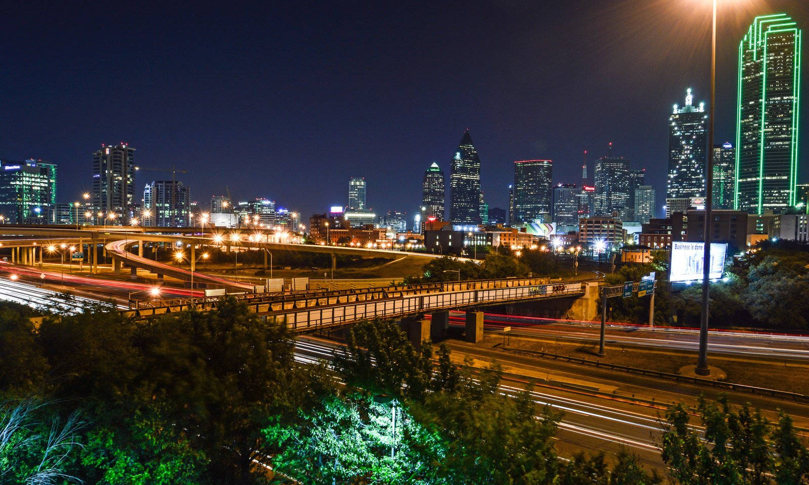 highway 桌布 壁紙 — 充滿活力的夜間城市景觀，有發光的摩天大樓和高架高速公路上的車流光跡。