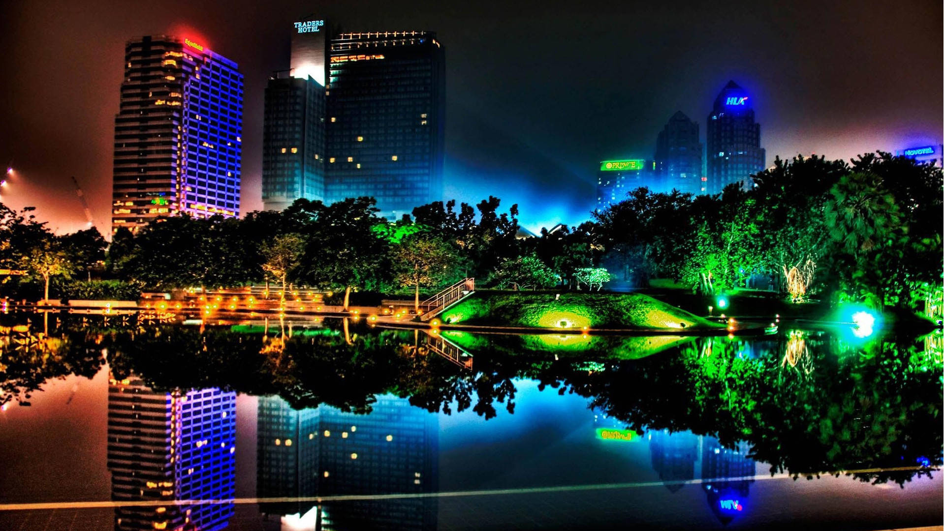 X 桌布 壁紙 — 充滿活力的夜間城市景觀，發光的摩天大樓倒映在平靜的湖面上，周圍環繞著發光的綠色樹木。