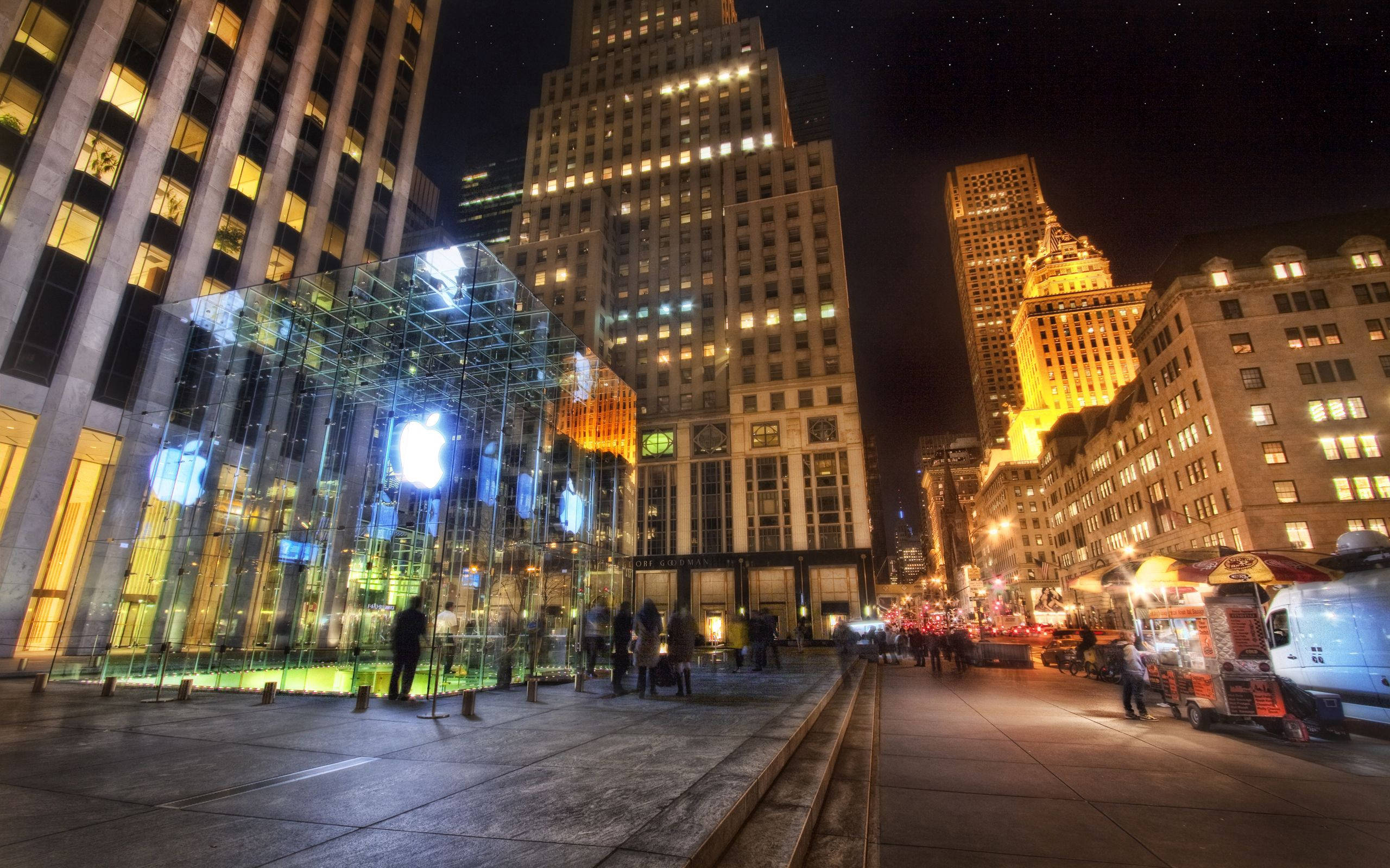 辦公室 桌布 壁紙 — 充滿活力的夜間城市景觀，發光的玻璃Apple Store矗立在燈火通明的摩天大樓和熙熙攘攘的街頭小販之間。