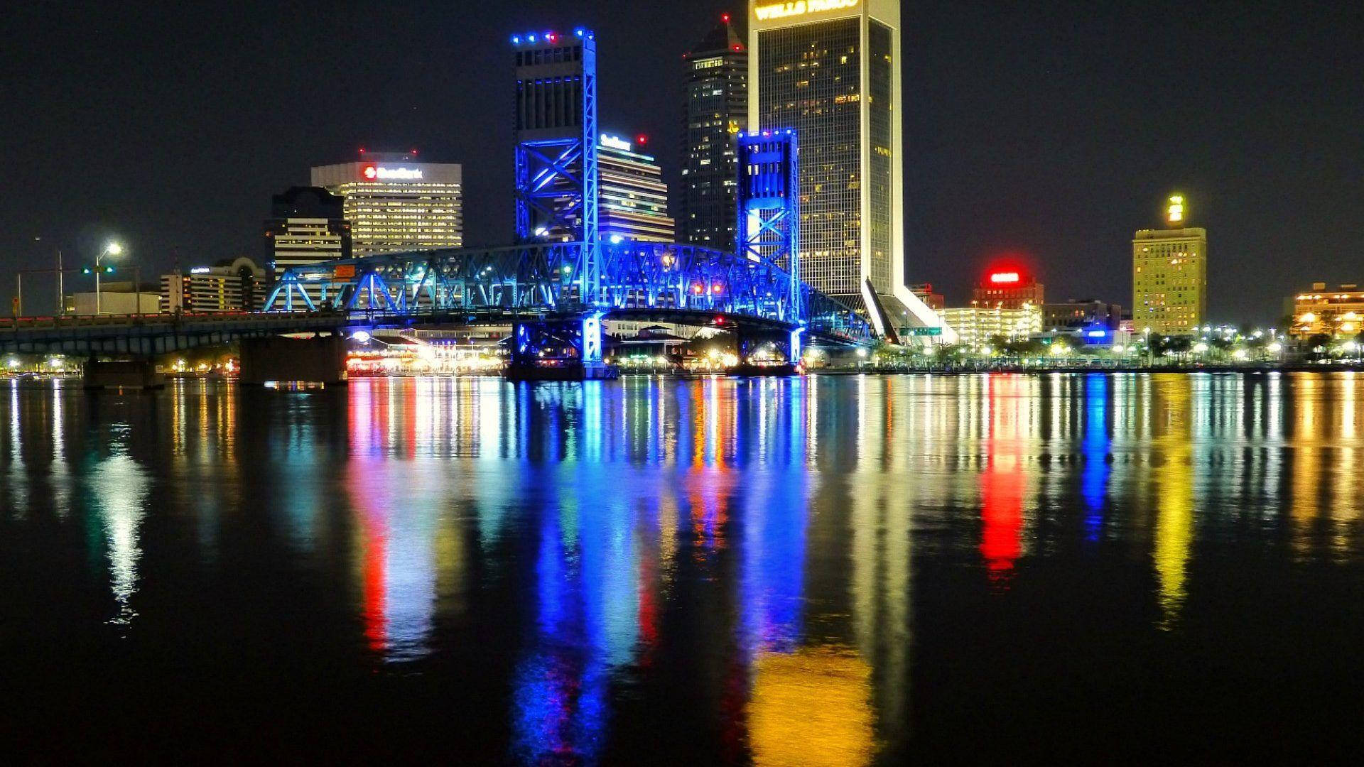 Jacksonville 桌布 壁紙 — 充滿活力的夜間城市景觀，發光的藍色橋樑和摩天大樓倒映在平靜的水面上。