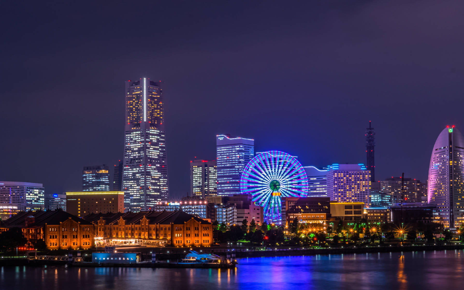 Yokohama 桌布 壁紙 — 充滿活力的夜間城市景觀，閃爍的摩天輪和摩天大樓倒映在平靜的水面上。