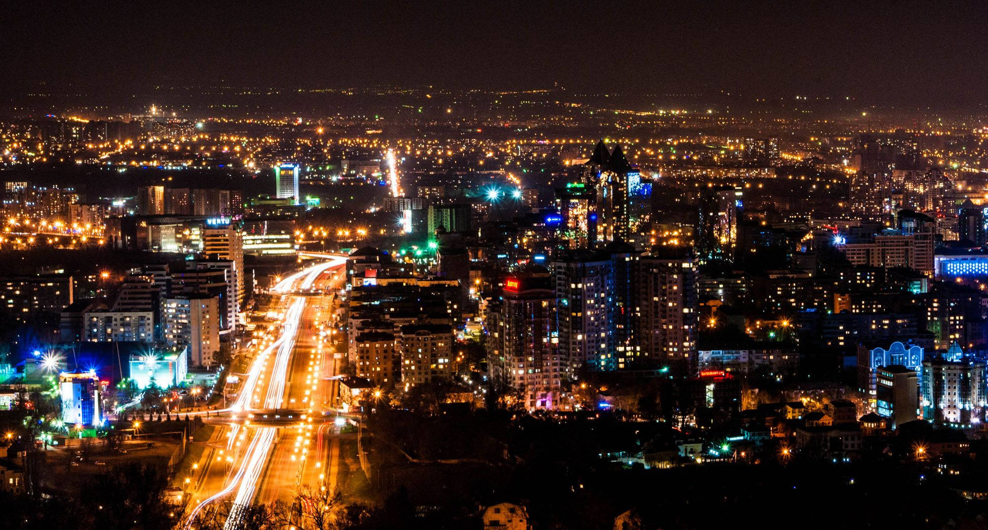 Kazakhstan 桌布 壁紙 — 充滿活力的夜間城市景觀，閃爍的摩天大樓和主要高速公路上的車流光跡。