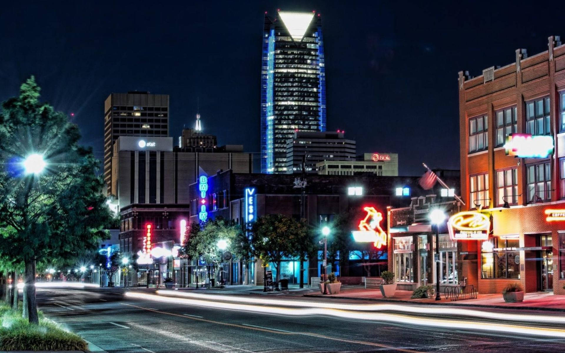 Oklahoma 桌布 壁紙 — 充滿活力的夜間城市景觀，閃爍的霓虹燈招牌和車流的光軌照亮了繁華的都市街道。
