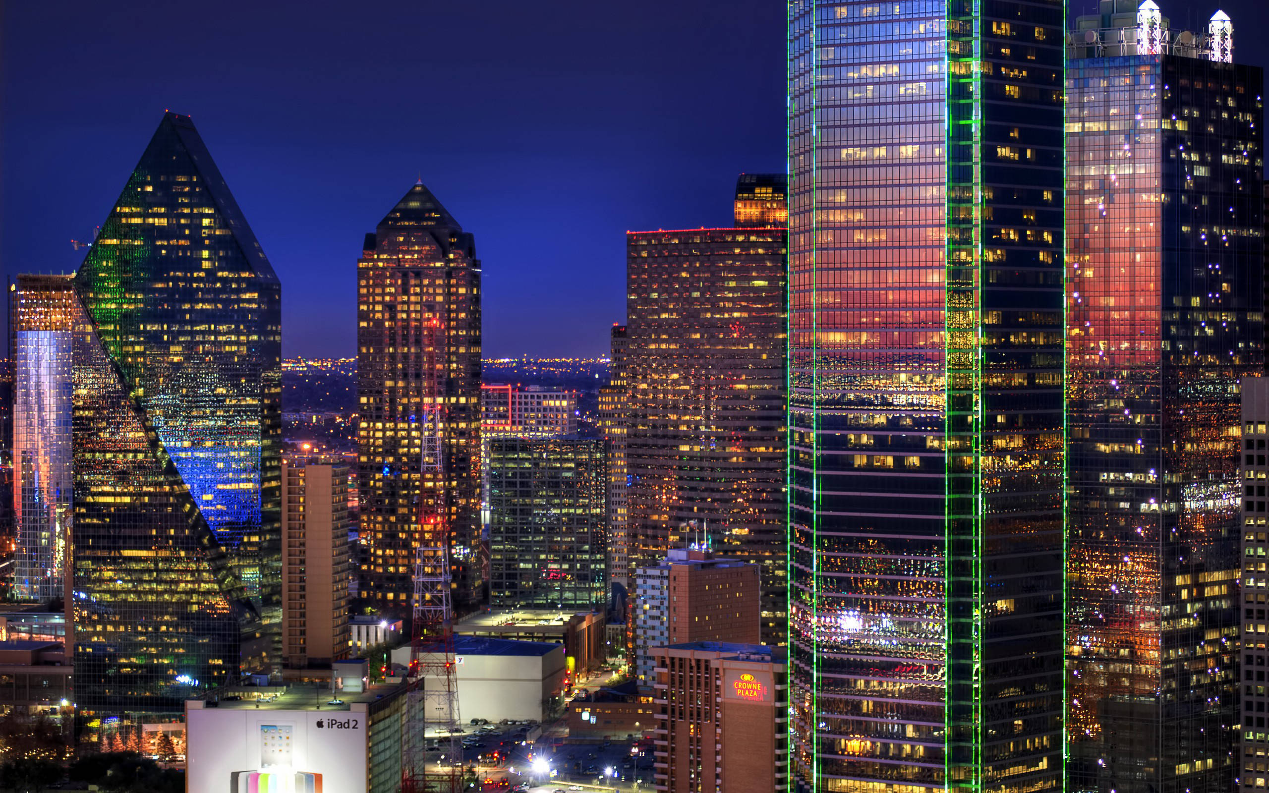 Dallas Skyline 桌布 壁紙 — 充滿活力的夜間城市景觀，高聳的摩天大樓在深藍色天空的映襯下閃爍著五彩繽紛的燈光。