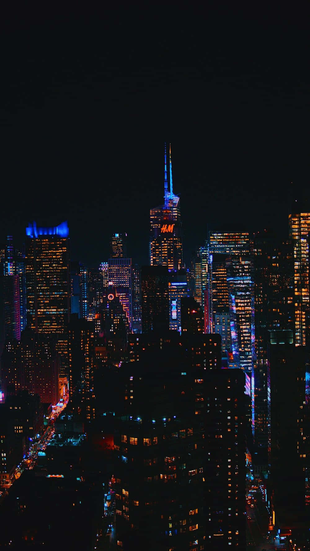 Ambience 桌布 壁紙 — 充滿活力的夜間城市景觀，高聳的摩天大樓在黑暗的天空中閃爍著霓虹燈光。