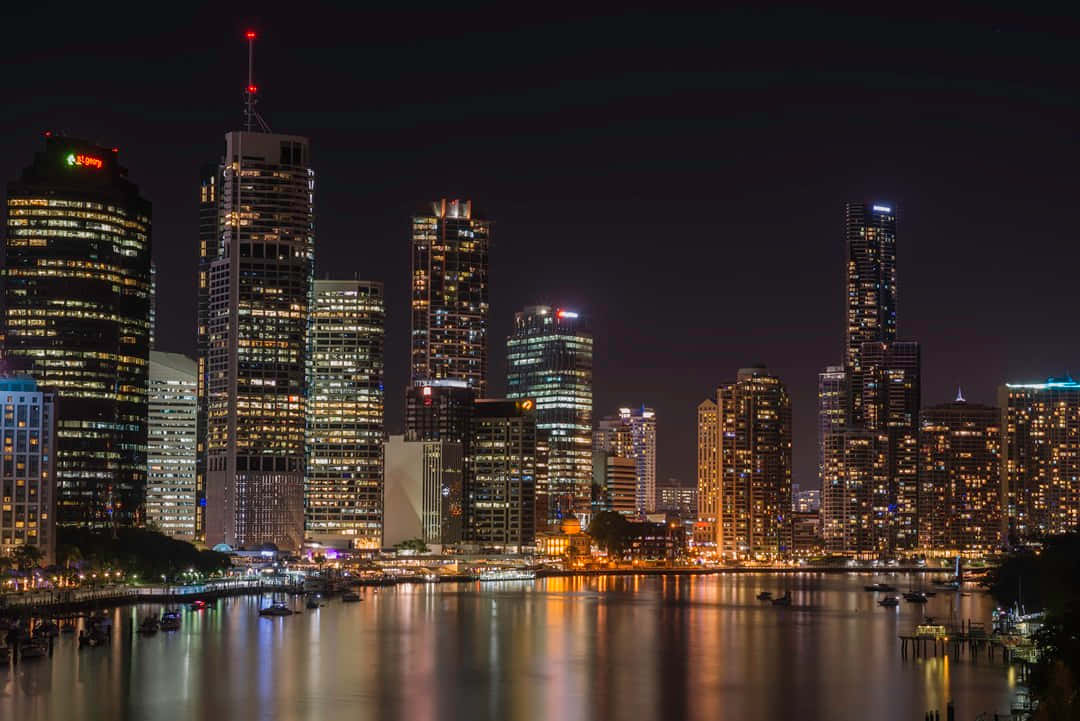 Adelaide 桌布 壁紙 — 充滿活力的夜間城市景觀，高聳的摩天大樓在平靜的河面上反射出金色的燈光。