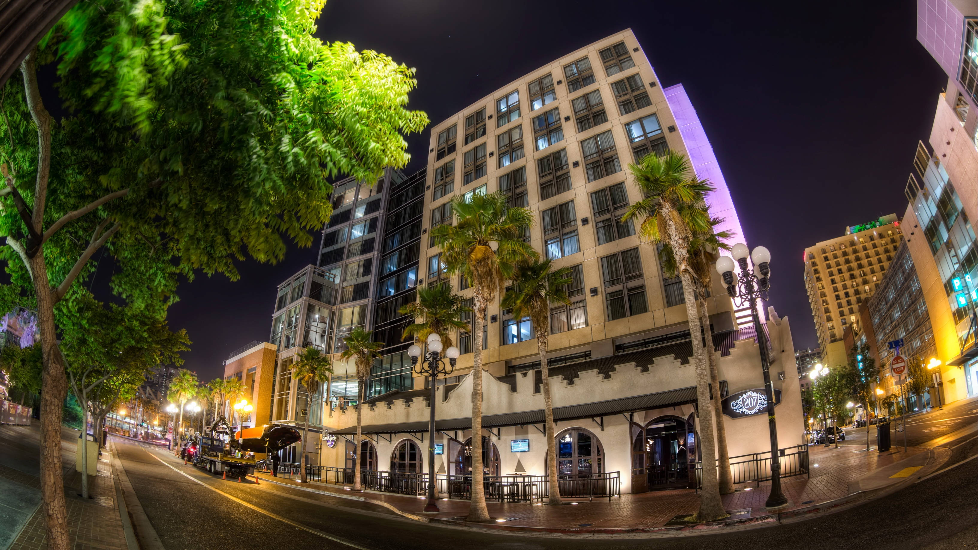 USA 桌布 壁紙 — 充滿活力的夜間城市街道場景，棕櫚樹在街燈和照明建築下閃耀。