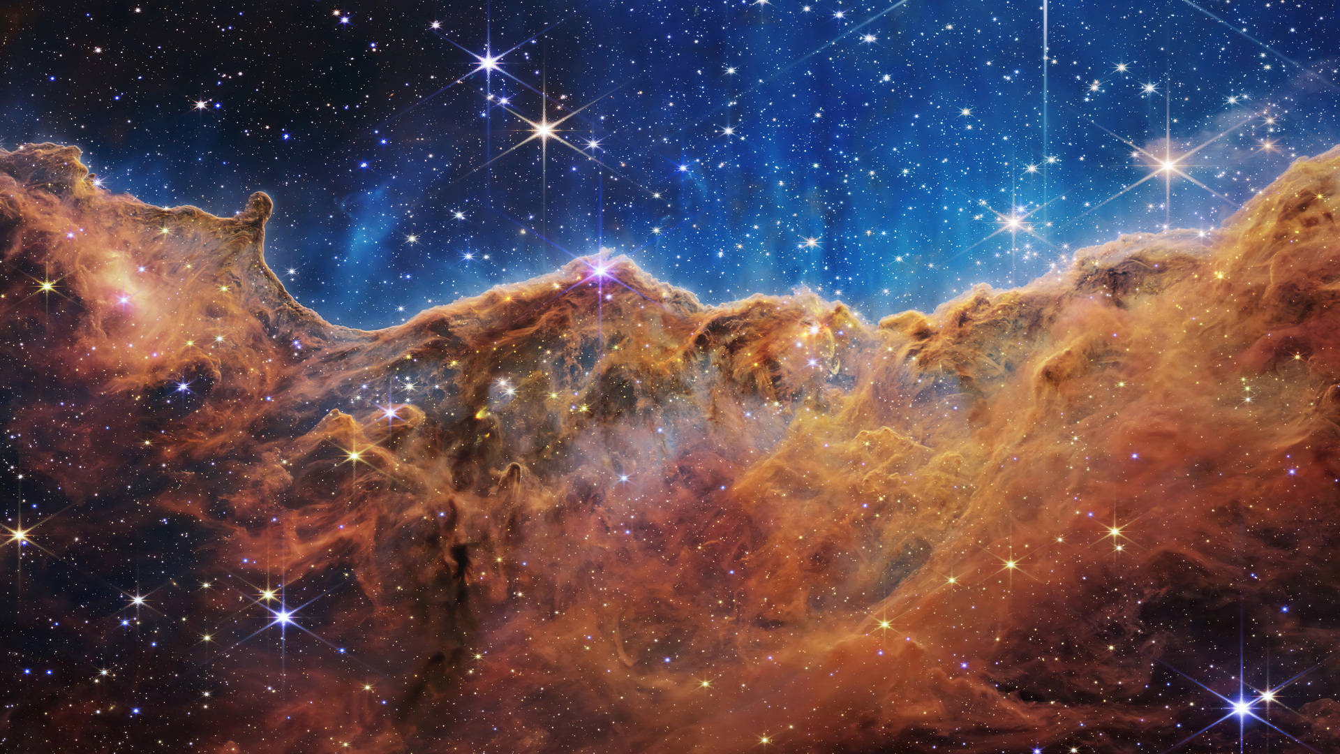 銀河 桌布 壁紙 — 充滿活力的宇宙星雲，在深藍色太空背景下，有發光的橙色雲朵和閃爍的星星。
