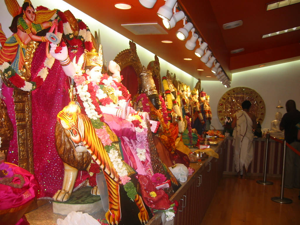 Indian 桌布 壁紙 — 充滿活力的寺廟內部，展示華麗的印度教神祇，飾以色彩繽紛的鮮花和金色點綴，在明亮的聚光燈下。