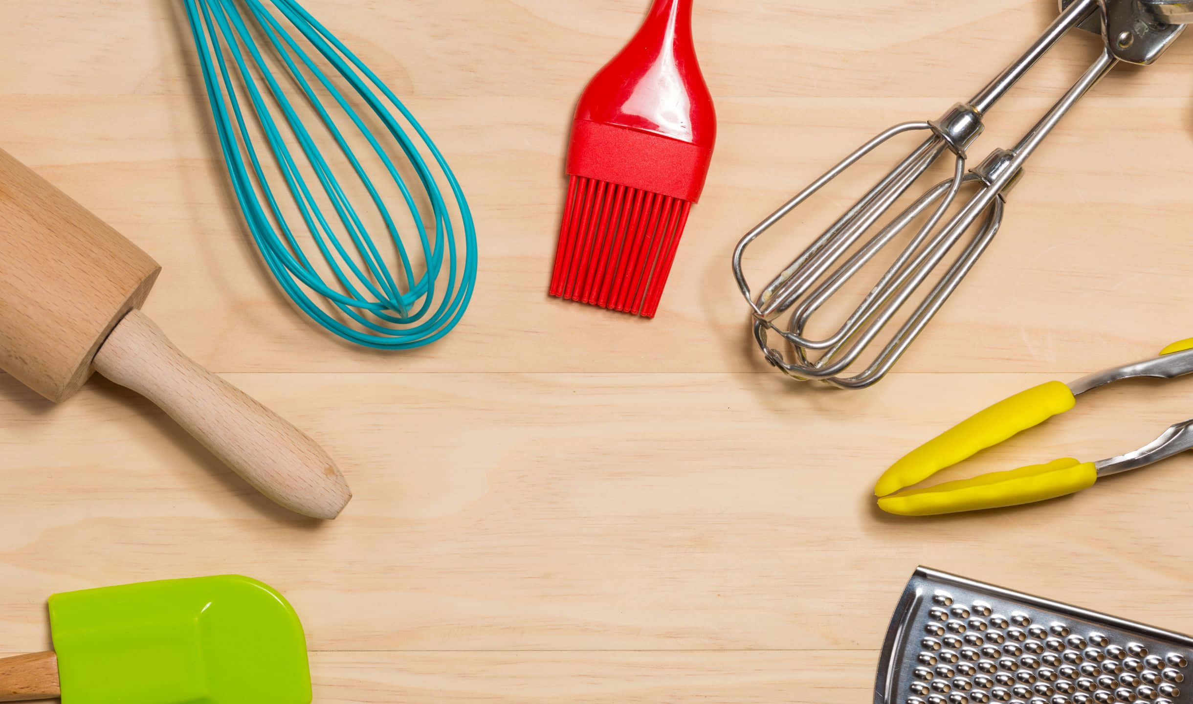kitchen 桌布 壁紙 — 充滿活力的廚房工具，如青綠色打蛋器、紅色刷子和黃色夾子，排列在淺色木質表面上。