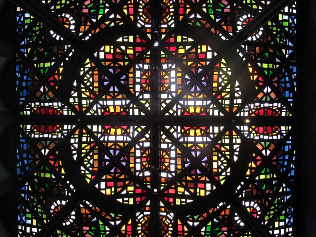 Theology 桌布 壁紙 — 充滿活力的彩色玻璃窗，幾何圖案透過深色金屬框架散發出繽紛光線。