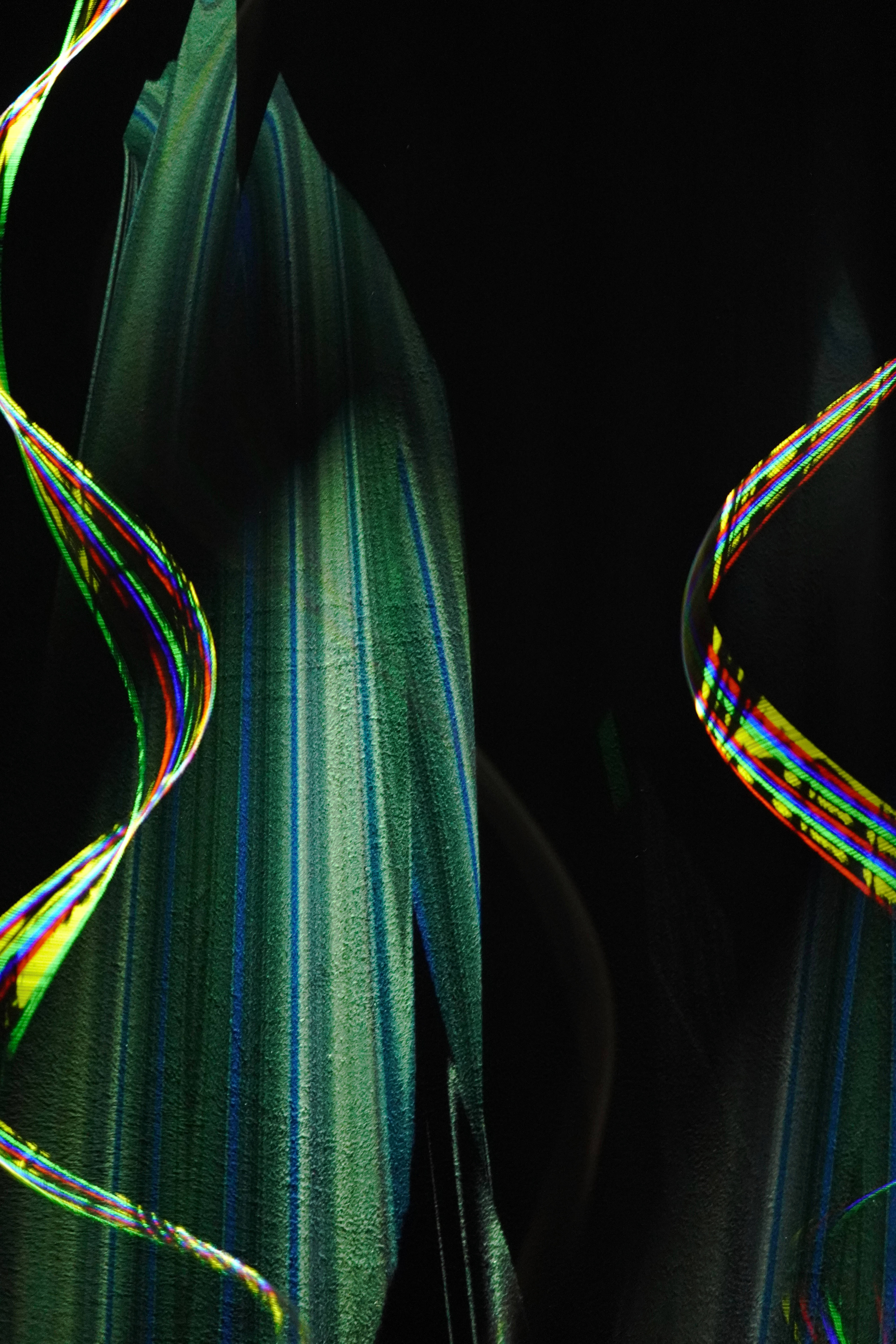 Illusion 桌布 壁紙 — 充滿活力的彩虹光跡在紋理綠色布料周圍旋轉，背景為純黑色。