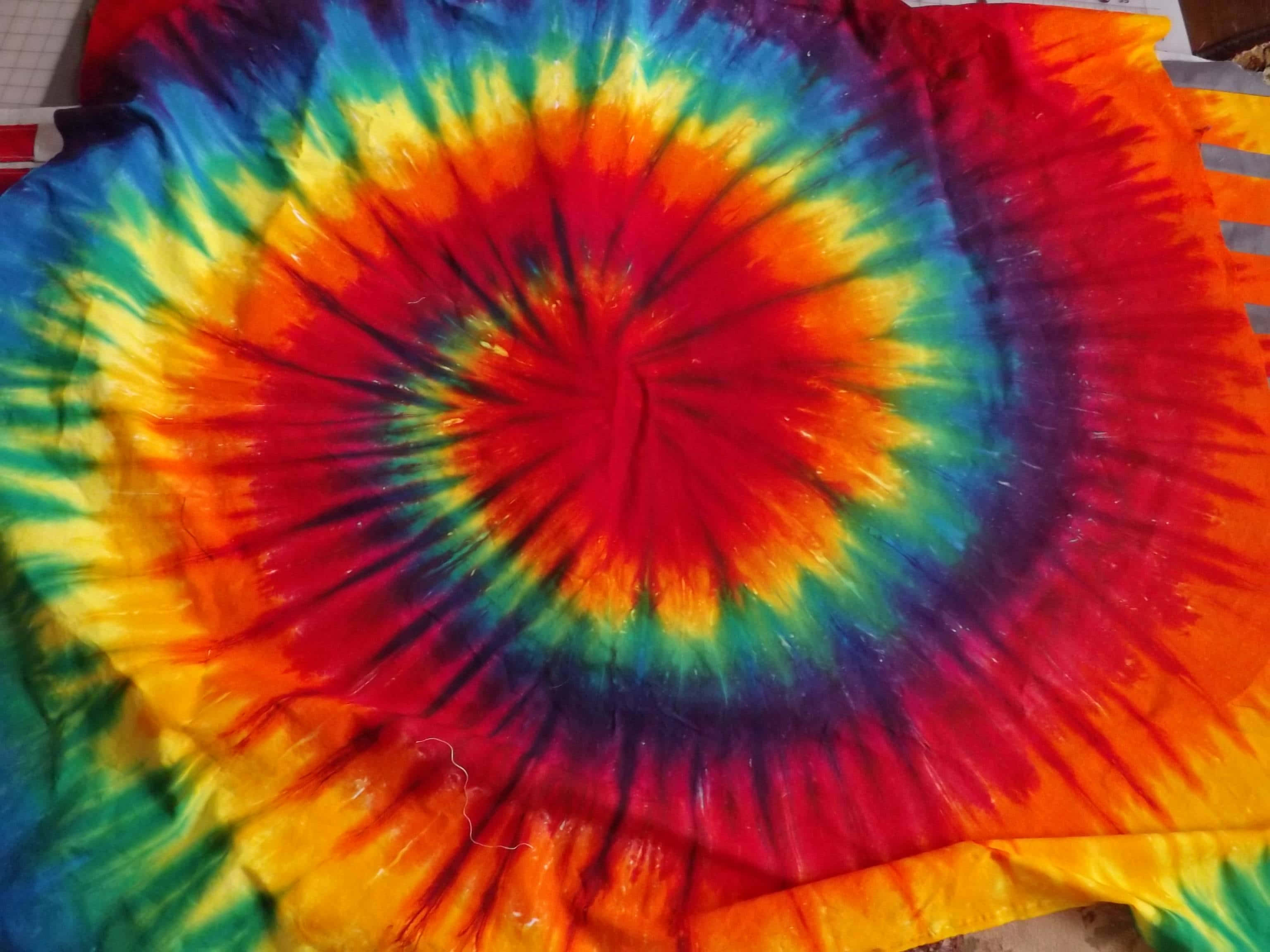 嬉皮 桌布 壁紙 — 充滿活力的彩虹螺旋紮染布料從火紅的中心向外輻射，帶有橙色、黃色、綠色和藍色的鮮明條紋。