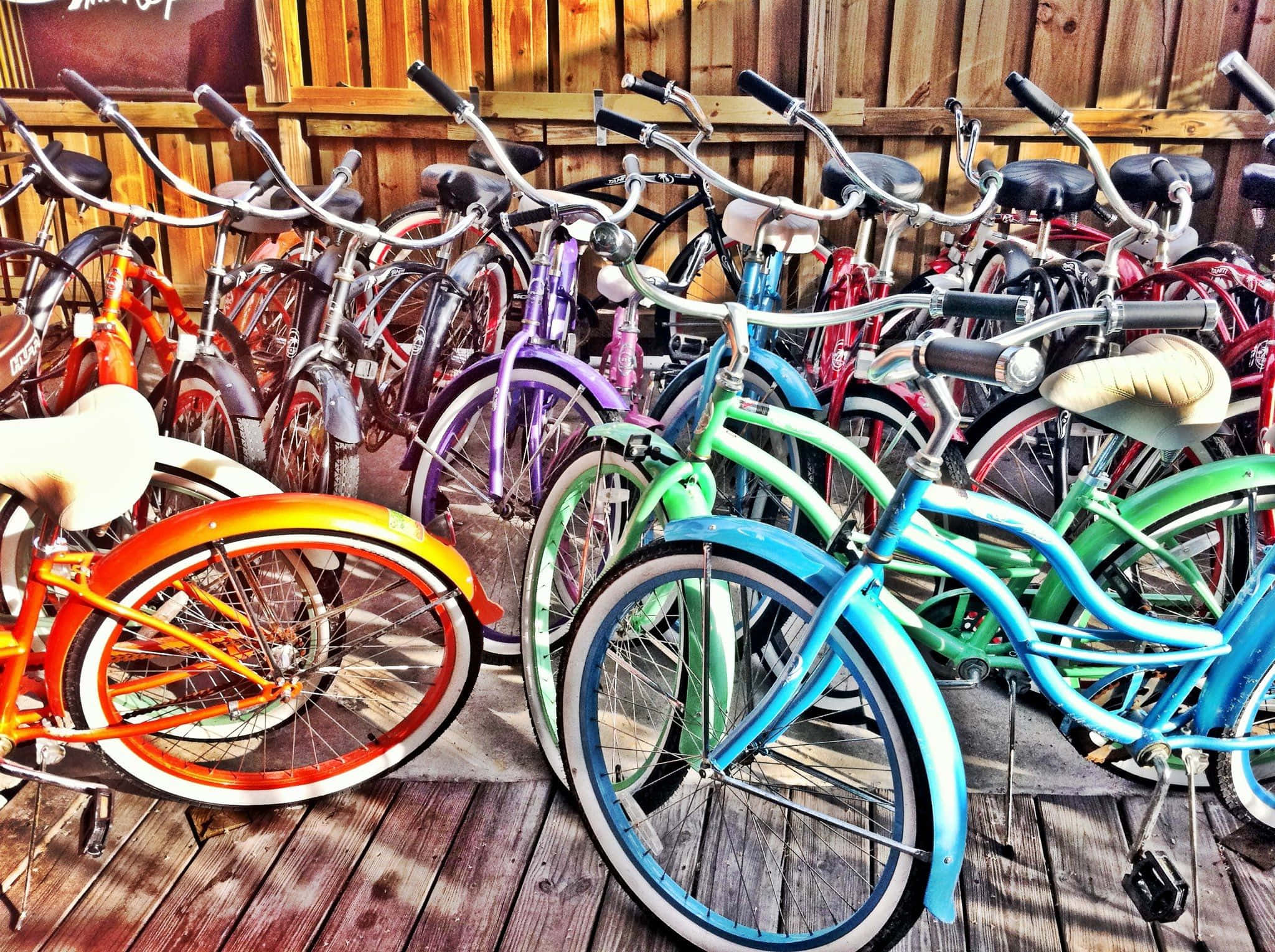 Beach Cruiser 桌布 壁紙 — 充滿活力的復古自行車以彩虹色調靠在陽光普照的甲板上的木柵欄上。