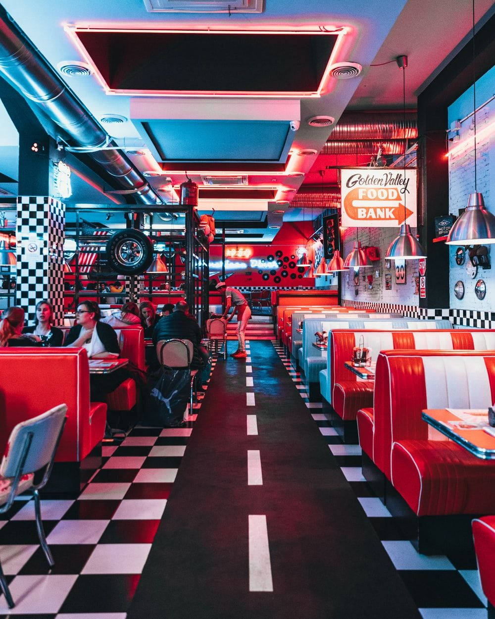 Diner 桌布 壁紙 — 充滿活力的復古餐廳，設有紅色卡座、棋盤格地板，霓虹燈在用餐的顧客身上投射出大膽的光芒。