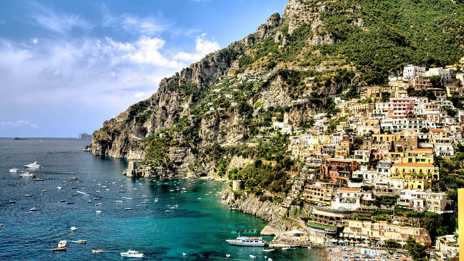 Italian Island 桌布 壁紙 — 充滿活力的懸崖小鎮波西塔諾依附在陡峭的綠色山脈上，俯瞰著點綴著船隻的碧綠海水，頭頂是明亮的藍天。