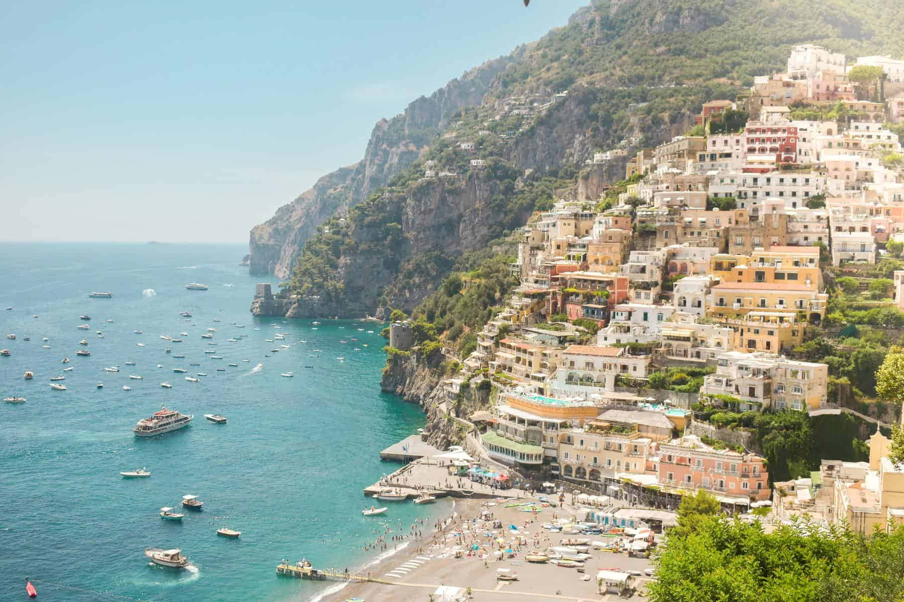 Italian Beach 桌布 壁紙 — 充滿活力的懸崖小鎮波西塔諾沿著陡峭的山坡傾瀉而下，進入點綴著船隻的碧綠海水，天空清澈湛藍。
