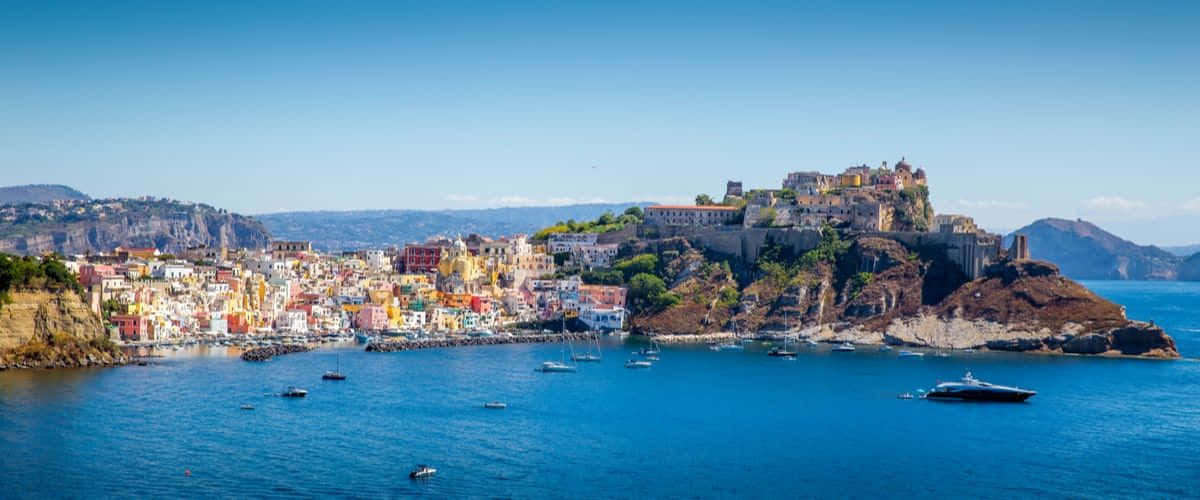 Italian Island 桌布 壁紙 — 充滿活力的懸崖村莊，粉彩房屋和小船點綴在清澈天空下的深藍色水域中。