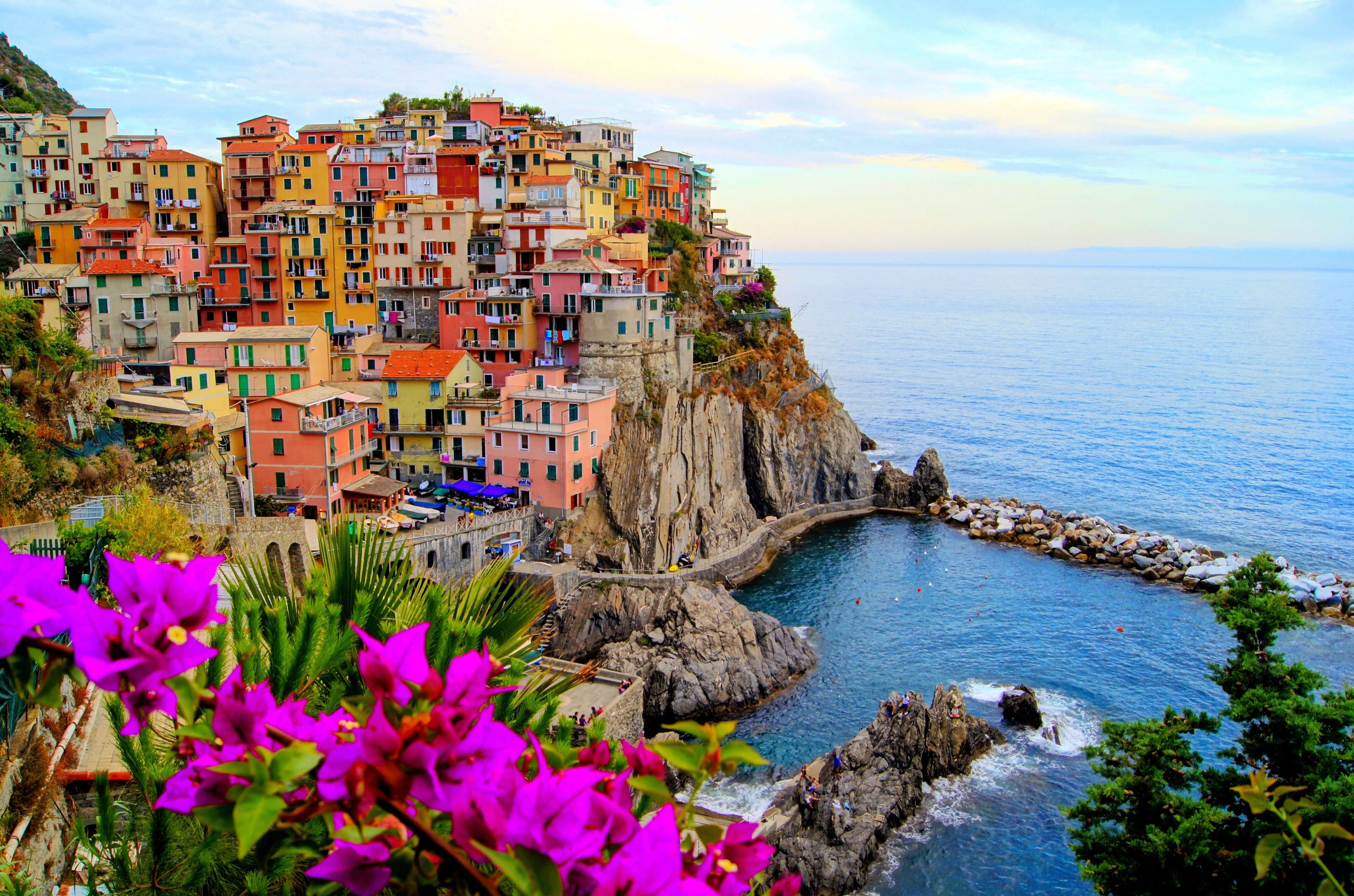 Italy Aesthetic 桌布 壁紙 — 充滿活力的懸崖村莊，粉彩房屋坐落在岩石海灣和碧綠海水之上，天空柔和。