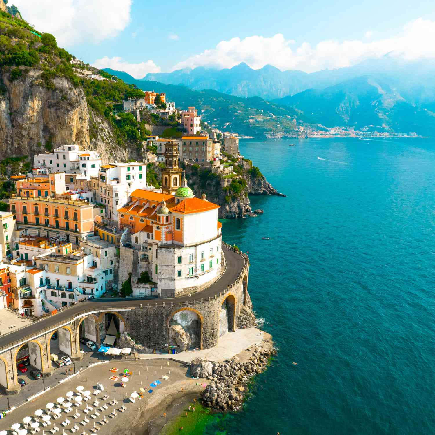 Italian Beach 桌布 壁紙 — 充滿活力的懸崖村莊，紅瓦屋頂緊貼岩石海岸，旁邊是碧綠色的海洋，在明亮的藍天下。