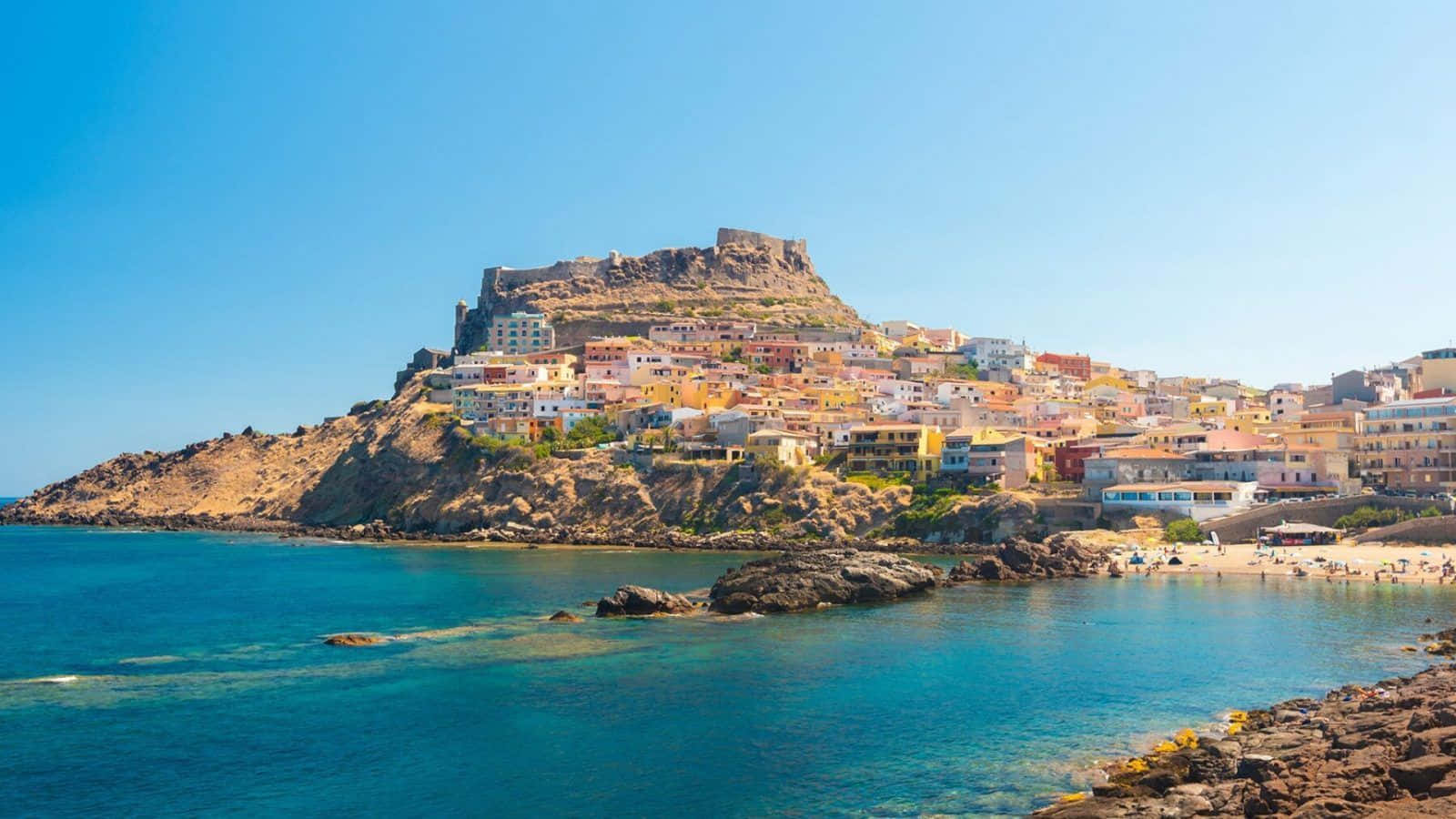 Italian Island 桌布 壁紙 — 充滿活力的懸崖村莊，色彩繽紛的房屋和古老堡壘矗立在碧綠色的海面上，晴空萬里。