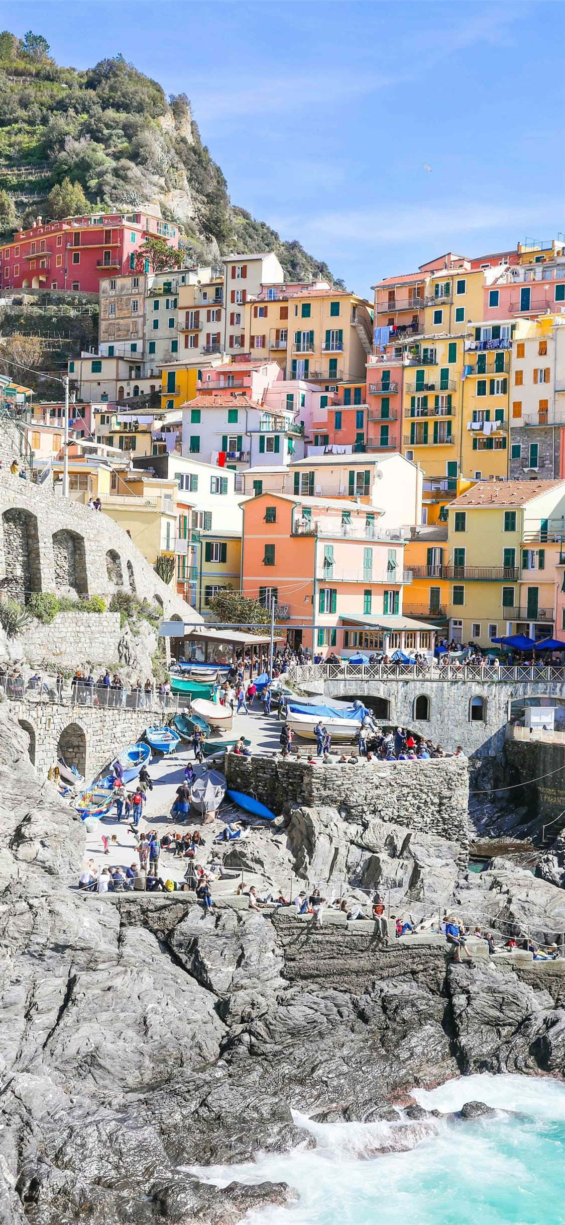 Italy Aesthetic 桌布 壁紙 — 充滿活力的懸崖村莊，色彩繽紛的房屋坐落在岩石海灣之上，海灣裡擠滿了人和船隻，天空清澈湛藍。