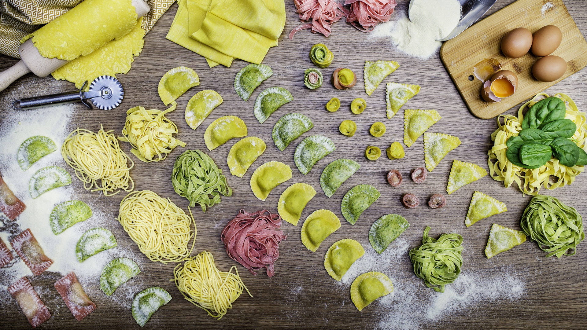 Pasta 桌布 壁紙 — 充滿活力的手工義大利麵，以黃色、綠色和粉紅色調藝術地擺放在撒滿麵粉的木桌上，配以新鮮羅勒和雞蛋。