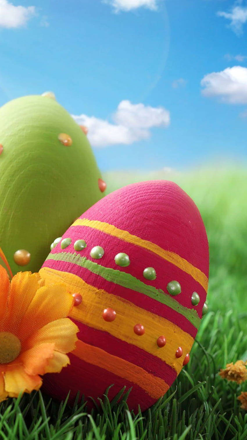 Easter Phone 桌布 壁紙 — 充滿活力的手繪復活節彩蛋帶有金屬飾釘，躺在茂密的綠草中，背景是明亮的藍天和蓬鬆的白雲。
