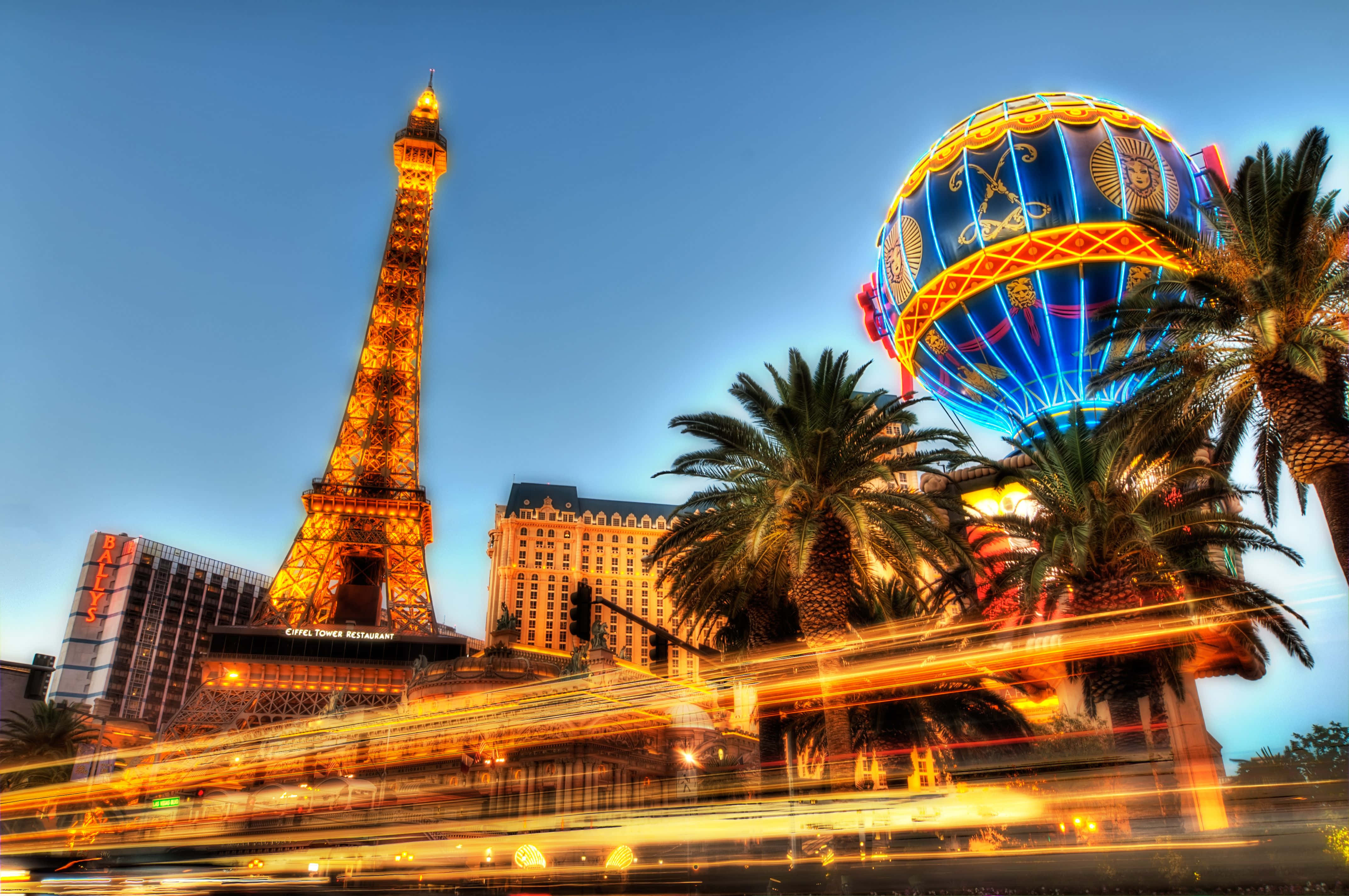 4K Las Vegas 桌布 壁紙 — 充滿活力的拉斯維加斯夜景，以棕櫚樹為框架，閃耀的艾菲爾鐵塔複製品和色彩繽紛的熱氣球雕塑。