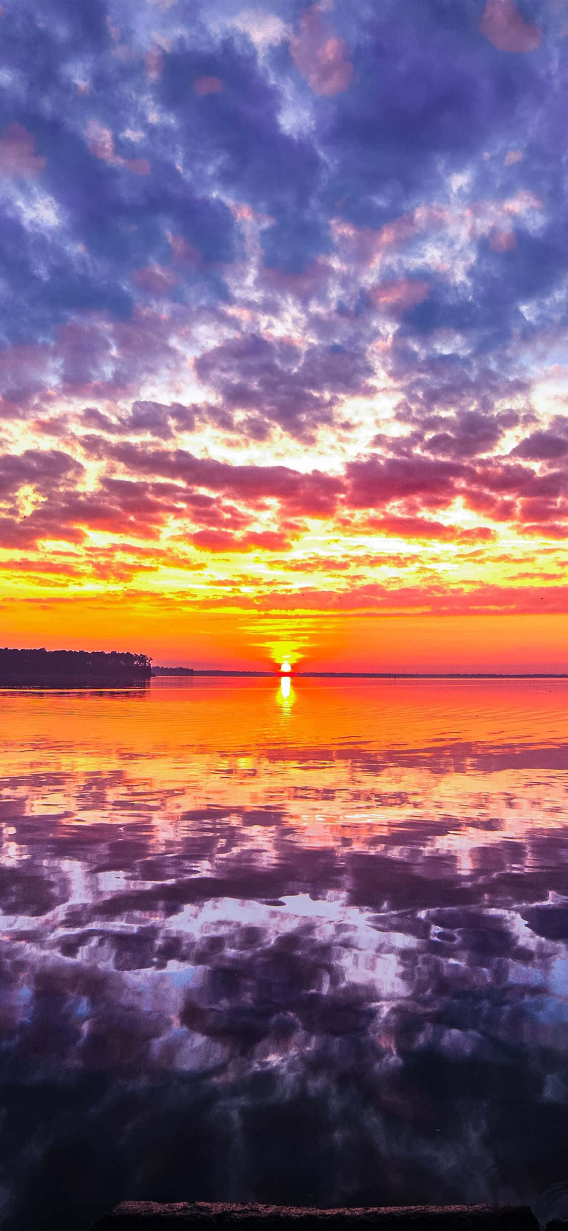 Sunset Beach iPhone 桌布 壁紙 — 充滿活力的日出將天空染成火熱的橙色和紫色雲彩，完美地倒映在平靜的湖面上。