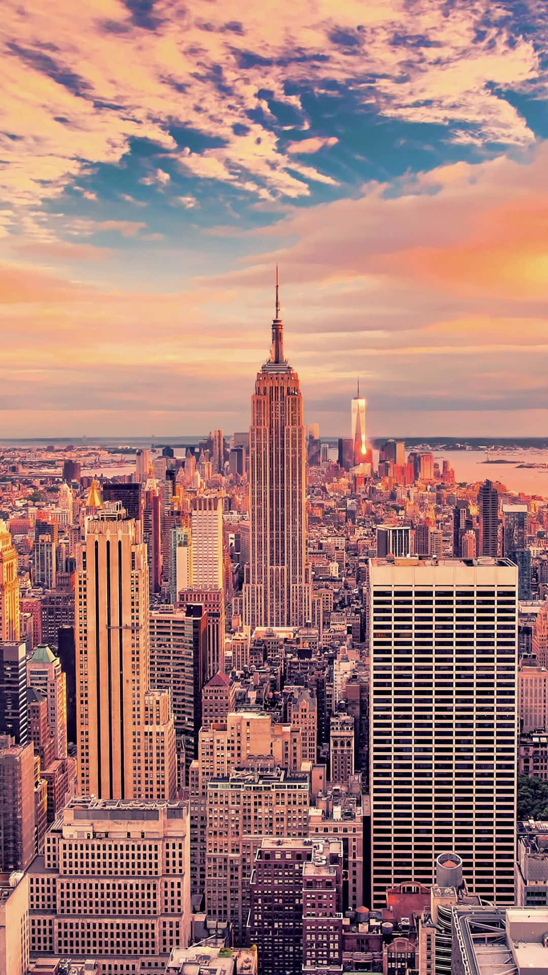 Android Ny City 桌布 壁紙 — 充滿活力的日落以溫暖的色調沐浴紐約市的天際線，帝國大廈聳立在密集的城市景觀之上。