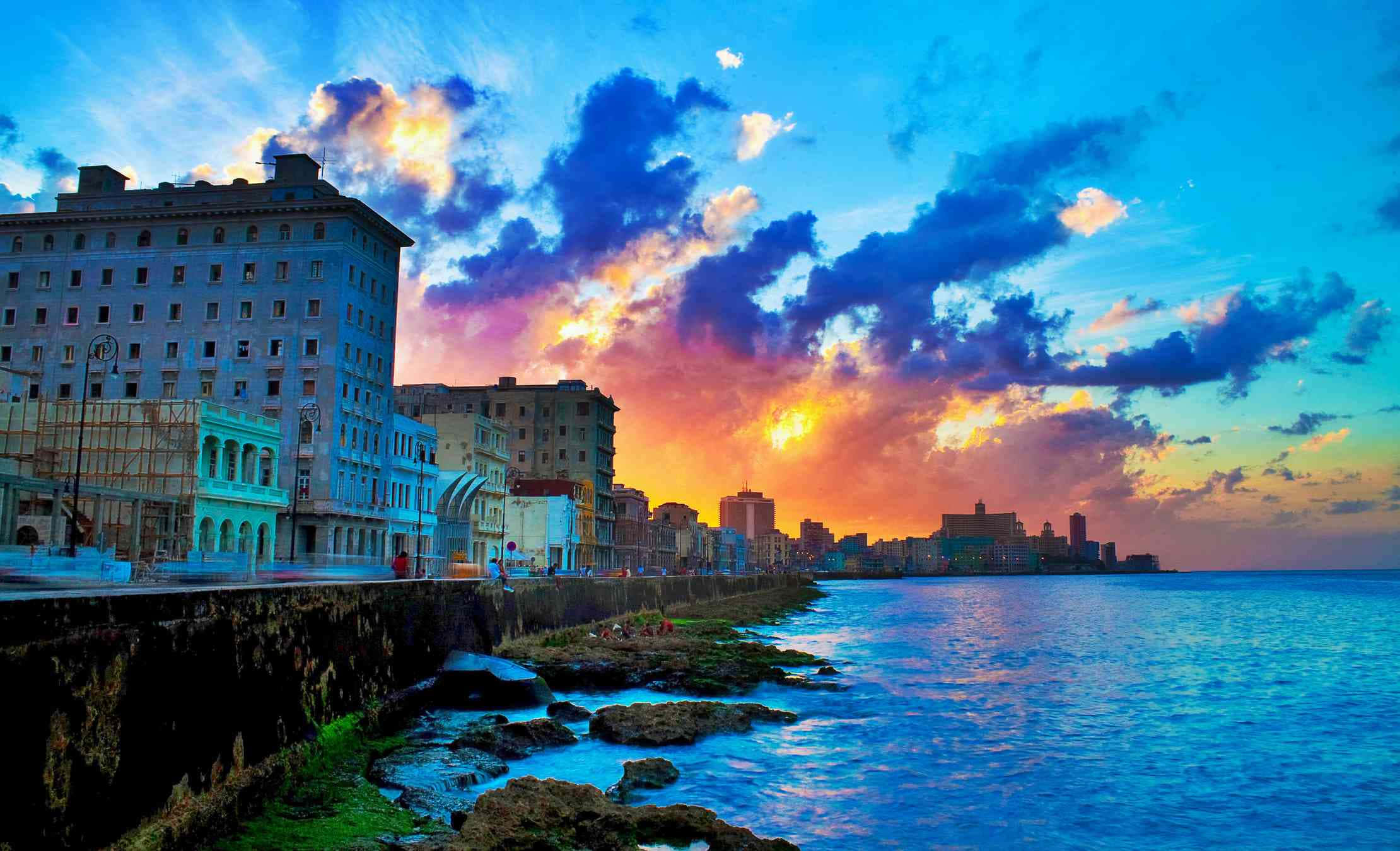 Cuba 桌布 壁紙 — 充滿活力的日落將哈瓦那的海岸天際線染成火橙色和深藍色的雲彩，映襯著歷史建築和碧綠的海水。