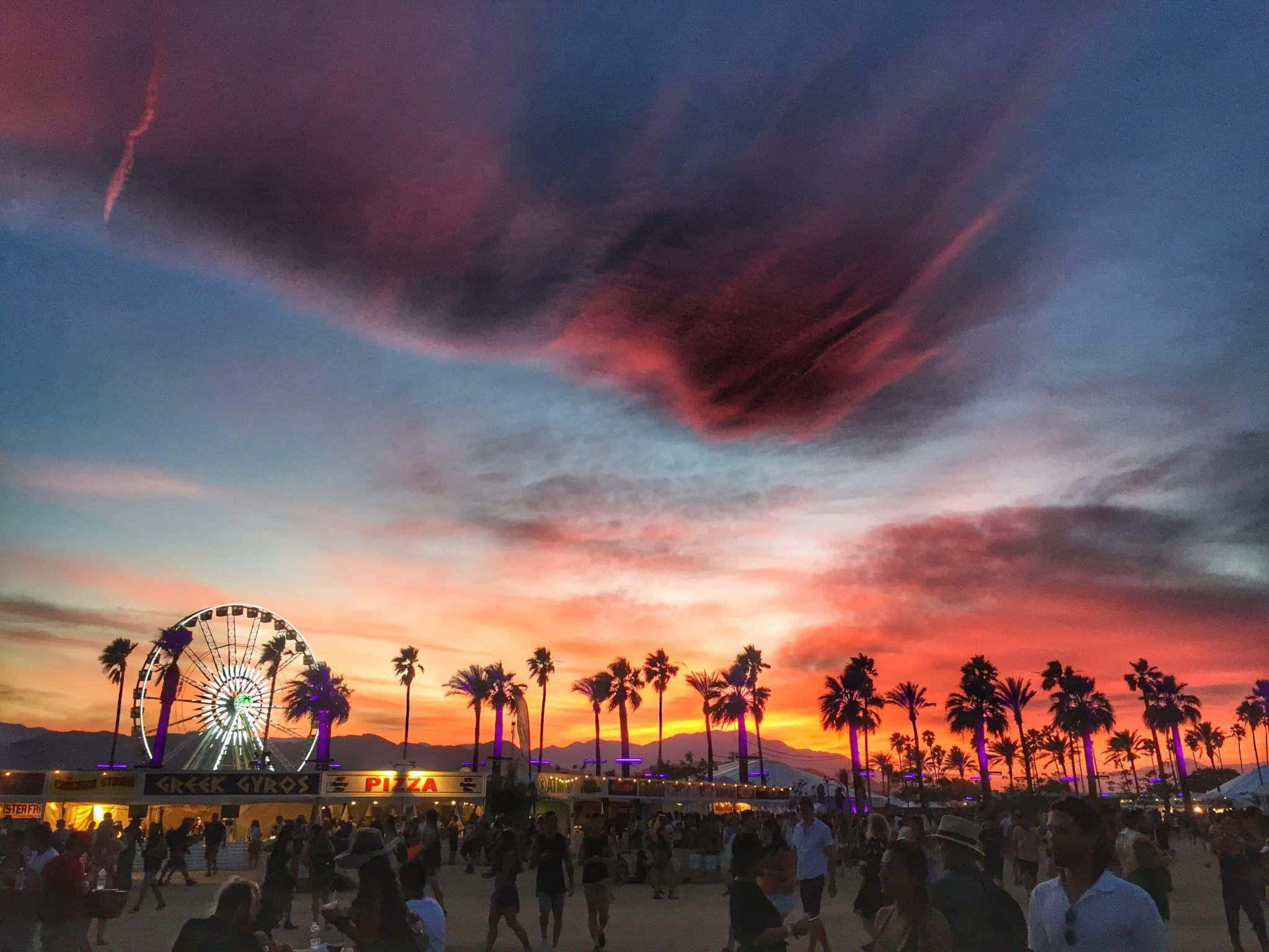 Coachella 桌布 壁紙 — 充滿活力的日落將天空染成火熱的橙色和紫色，映照在棕櫚樹和閃閃發光的摩天輪之上的熱鬧節日。