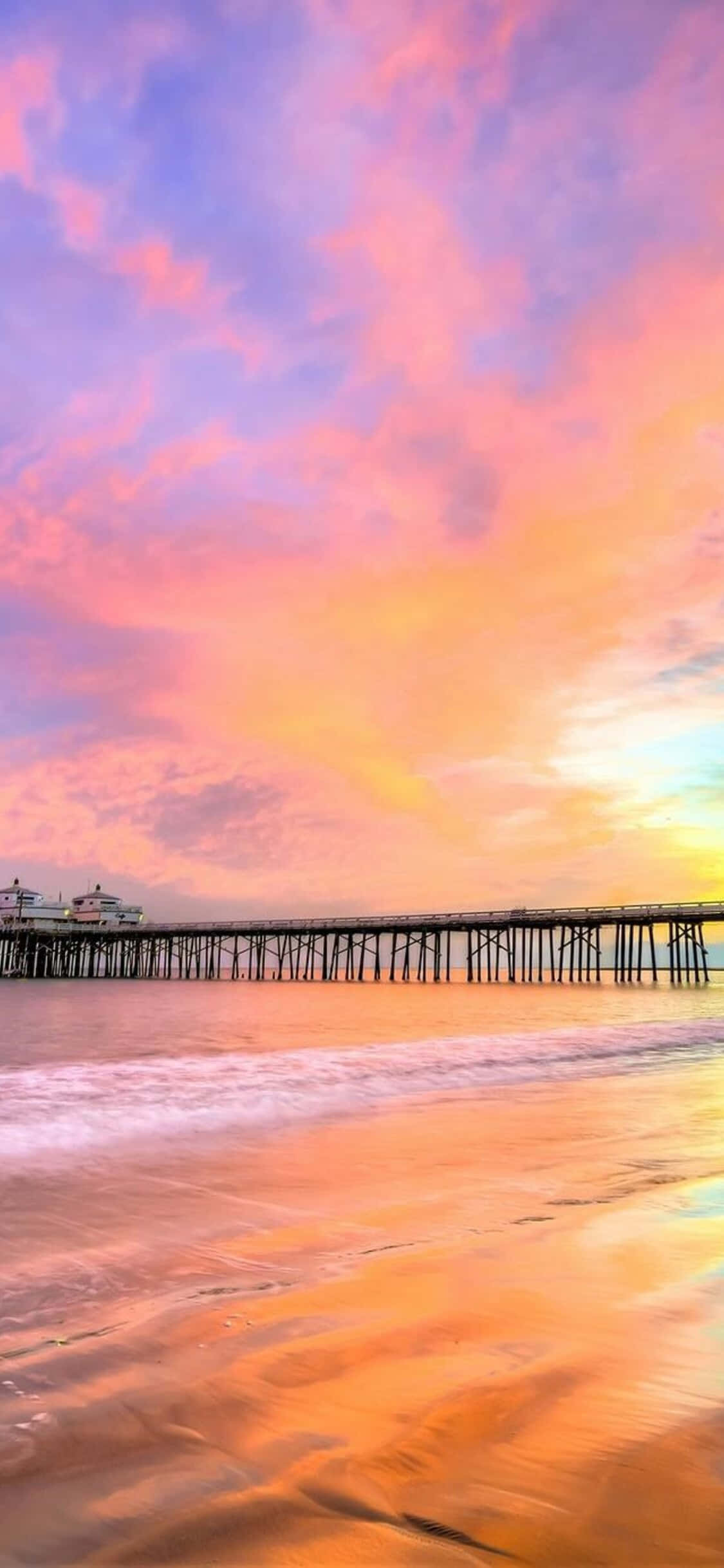 Pier 桌布 壁紙 — 充滿活力的日落將天空染成粉紅色、橙色和紫色，映照在延伸至平靜海面的長長碼頭之上。