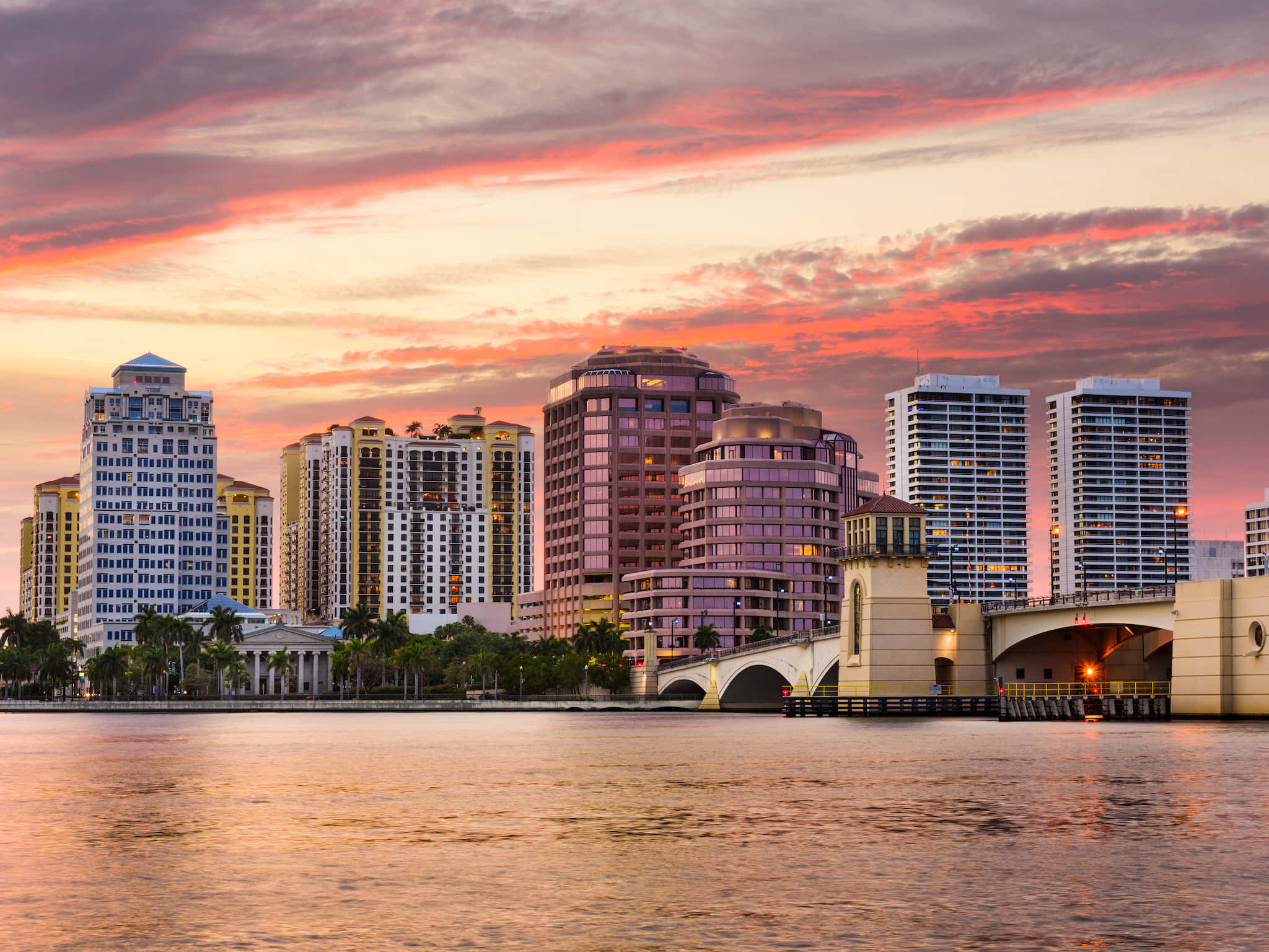 florida 桌布 壁紙 — 充滿活力的日落將天空染成粉紅色和橙色的色調，映照在平靜水面上的現代城市天際線之上。