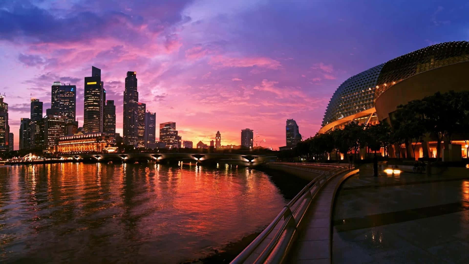 Singapore 桌布 壁紙 — 充滿活力的日落將新加坡天際線染成粉紅色和紫色，倒映在下面的河流中。