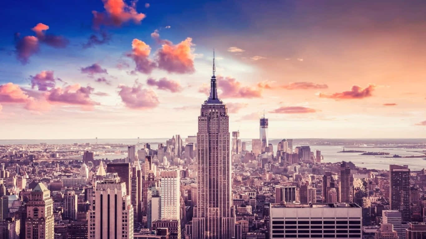 1366x768 Empire State Building 桌布 壁紙 — 充滿活力的日落將標誌性的帝國大廈和紐約市天際線沐浴在溫暖的粉紅色和橙色色調中。