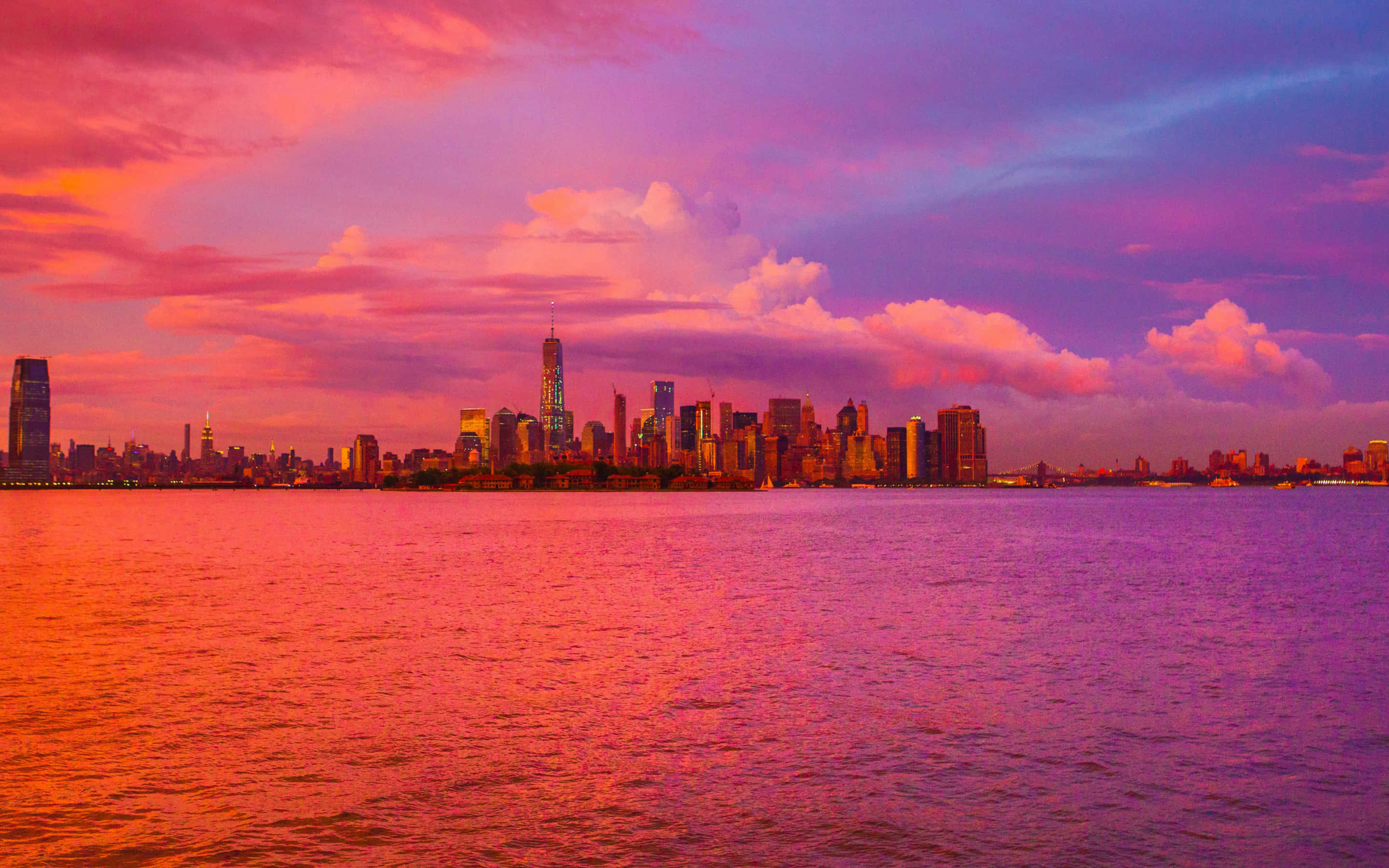 New York City 4K Ultra HD 桌布 壁紙 — 充滿活力的日落將紐約市天際線染成粉紅色和紫色調，倒映在下方平靜的水面上。