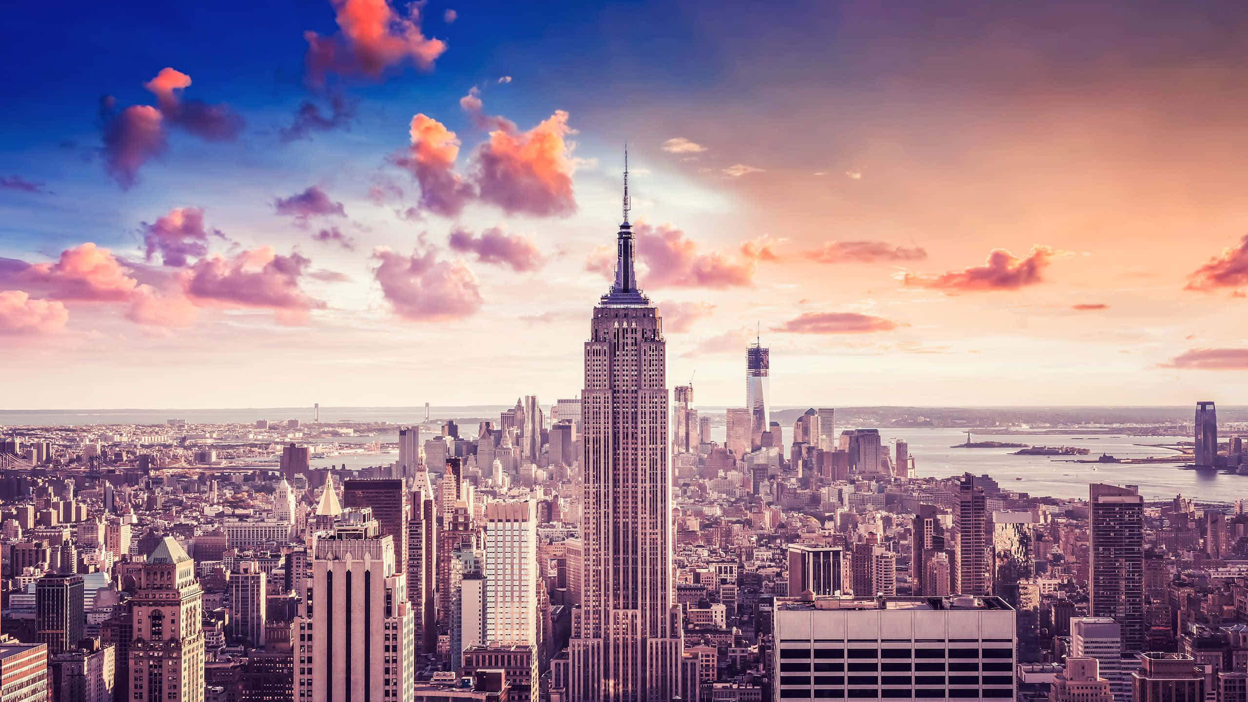 New York State 桌布 壁紙 — 充滿活力的日落將紐約市天際線染成粉紅色和金色色調，帝國大廈聳立在城市景觀之上。