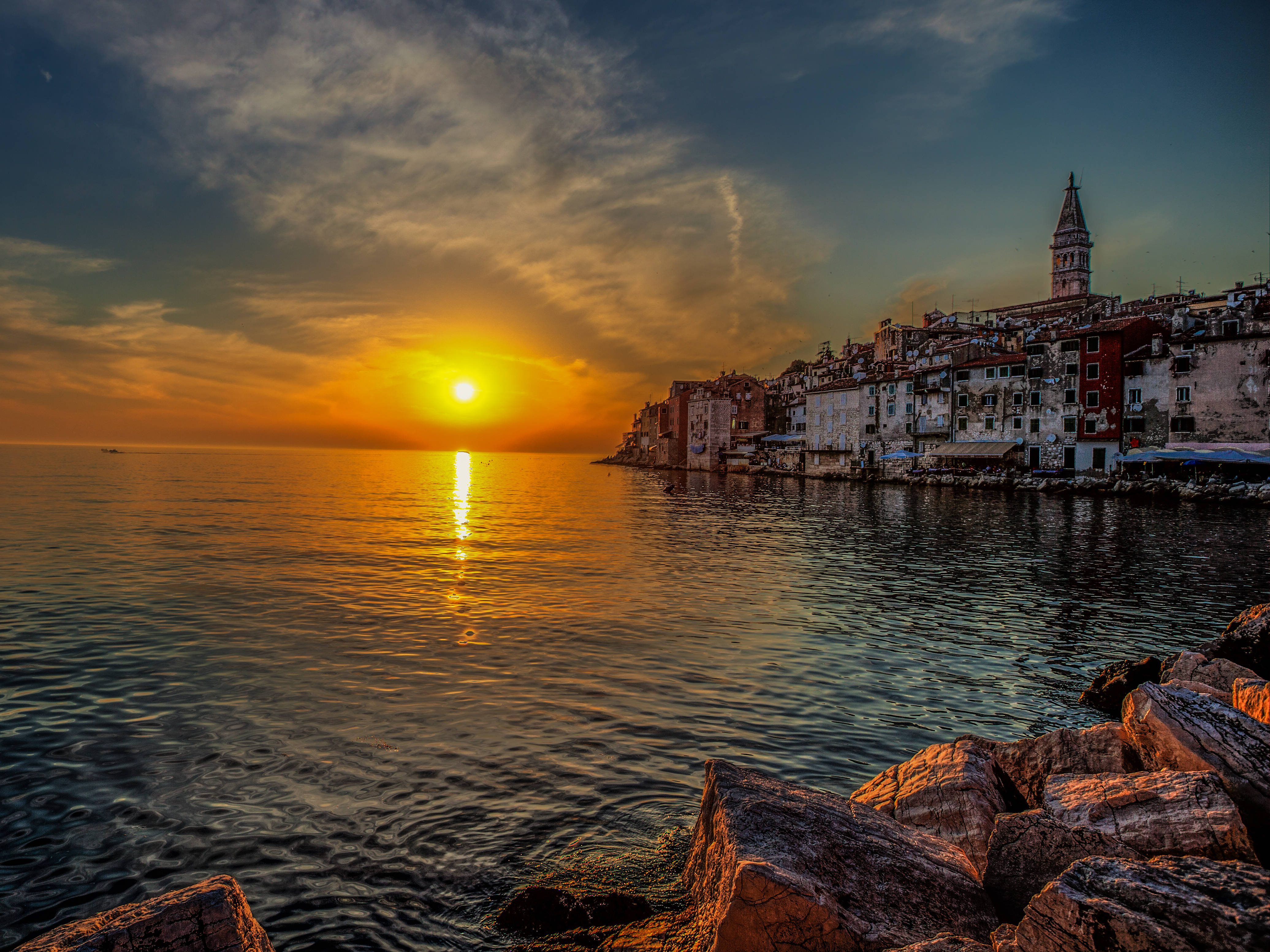 Croatia 桌布 壁紙 — 充滿活力的日落將金色光芒灑在平靜的水面上，歷史悠久的沿海建築在戲劇性的天空下聳立。
