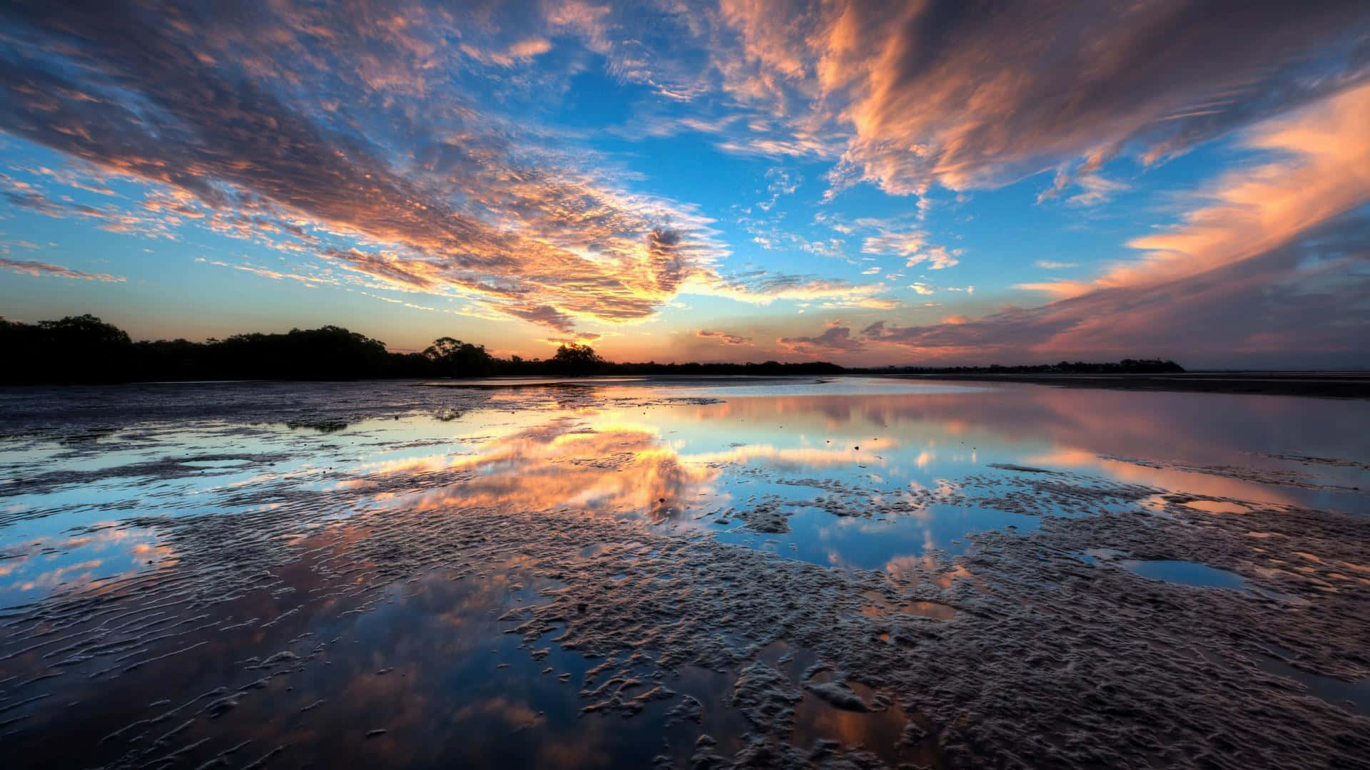 Sunset Reflection 桌布 壁紙 — 充滿活力的日落用火熱的橙色和紫色描繪天空，完美地反射在淺淺的、有紋理的濕地中。