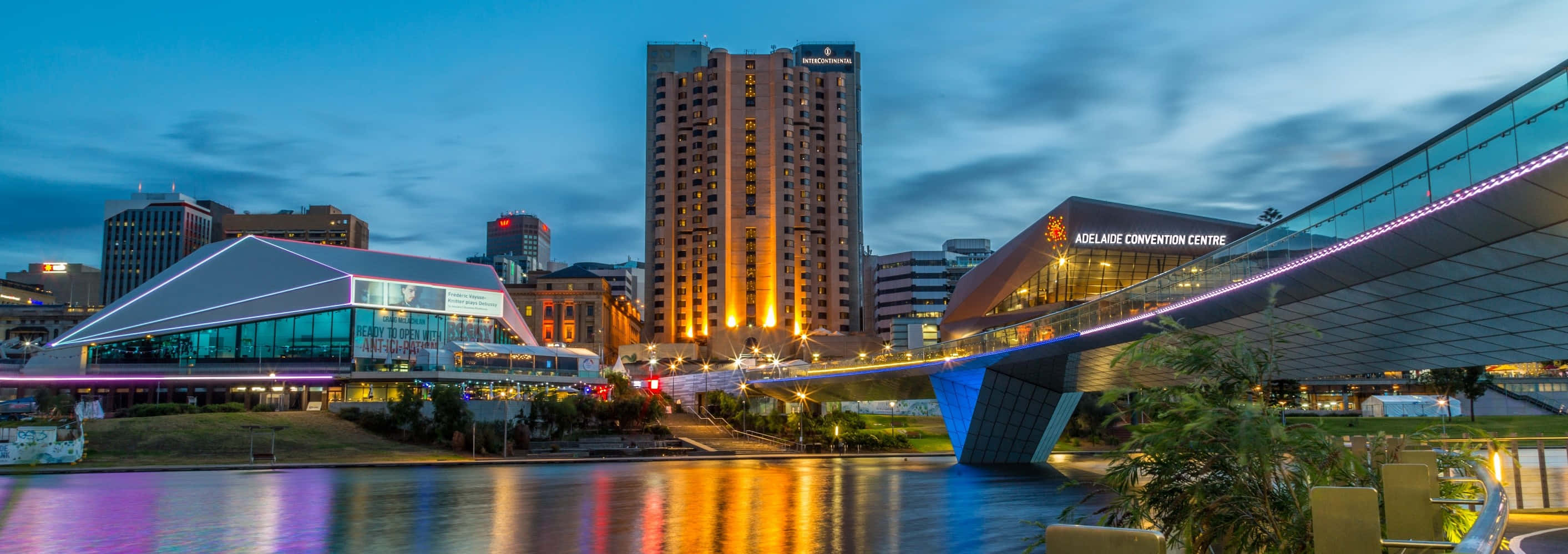 Adelaide 桌布 壁紙 — 充滿活力的暮色城市景觀，現代建築與發光的橋樑倒映在平靜的水面上。
