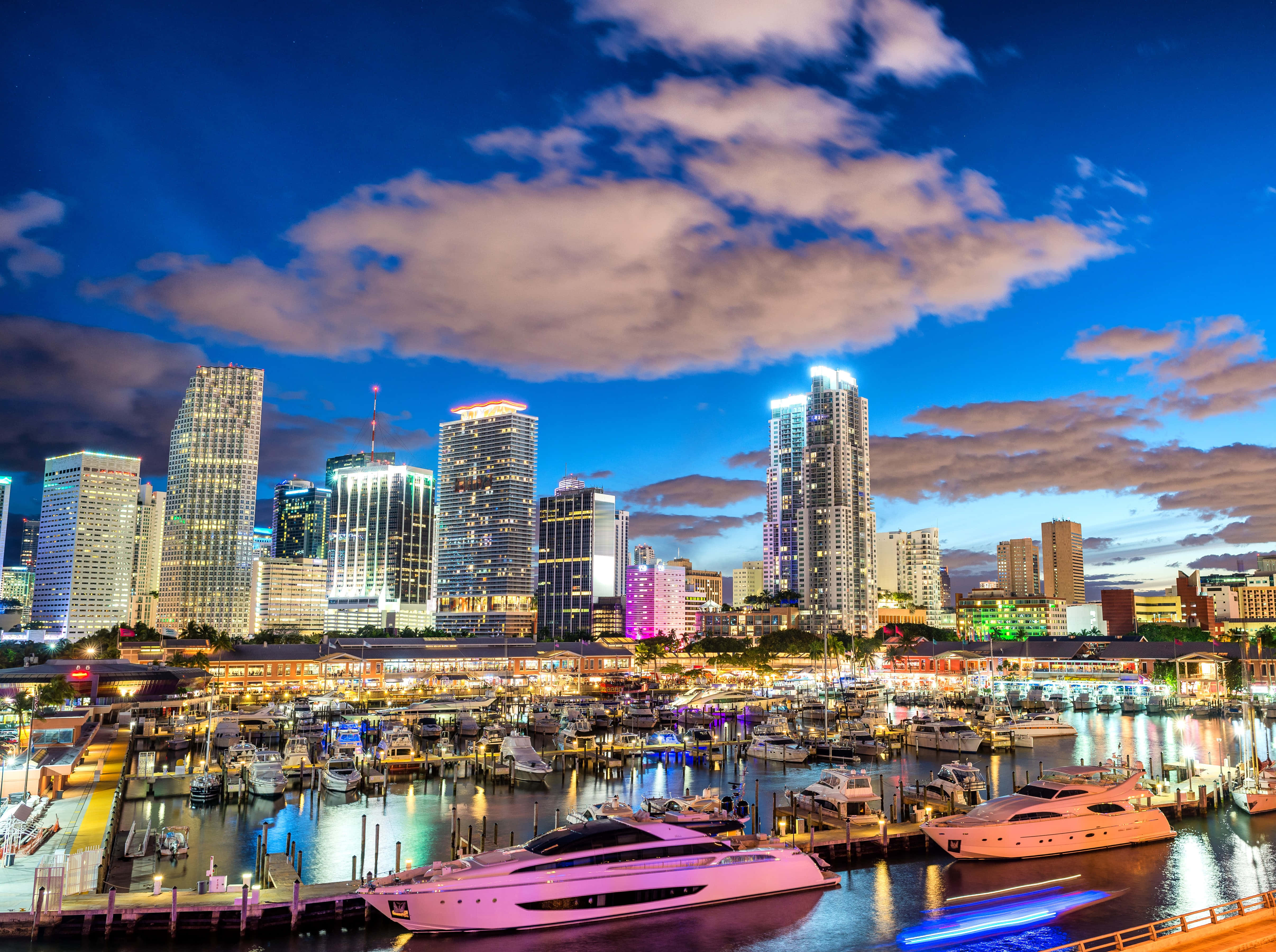 Miami 4K 桌布 壁紙 — 充滿活力的暮色城市景觀，閃爍的摩天大樓和豪華遊艇停泊在繁忙的港口，天空呈現戲劇性的藍色。