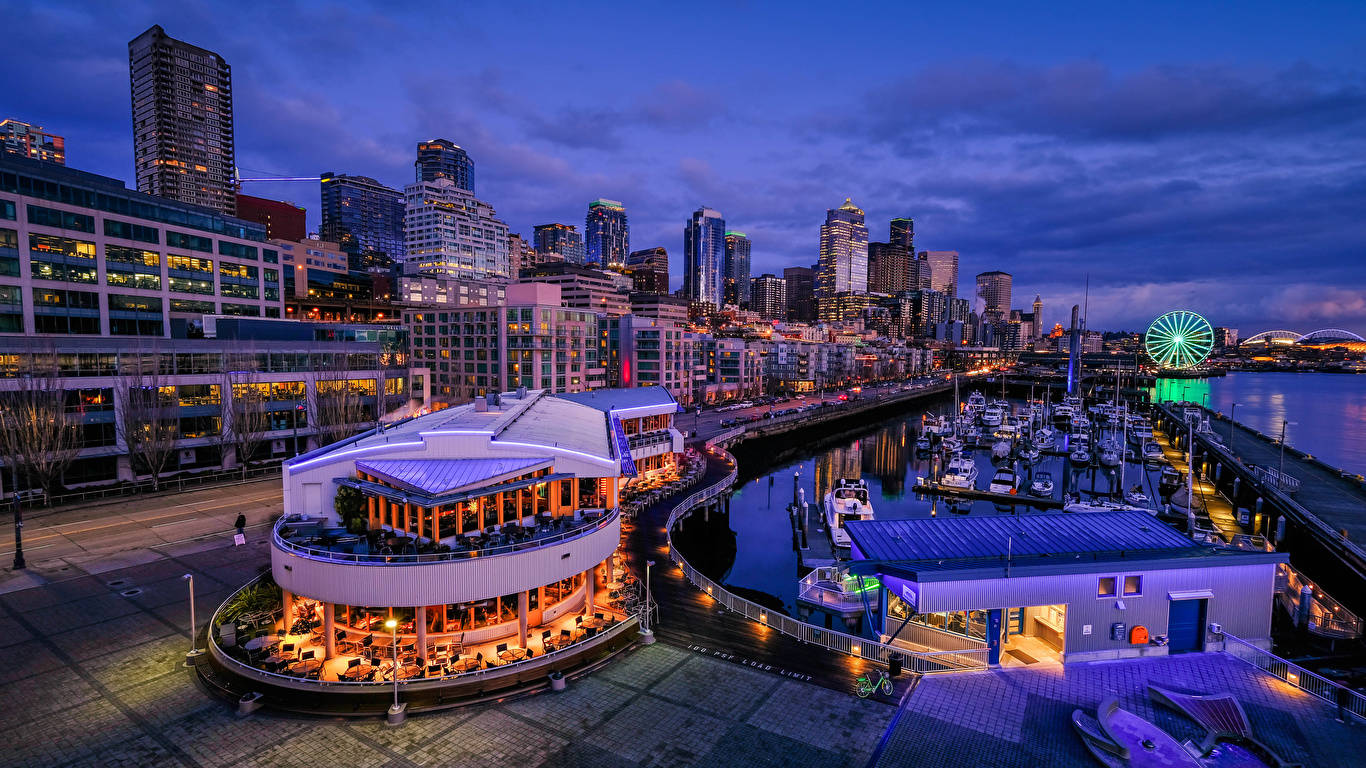 Seattle 桌布 壁紙 — 充滿活力的暮色城市景觀，閃爍的摩天大樓、海濱餐廳和發光的摩天輪在平靜的水面上倒映。