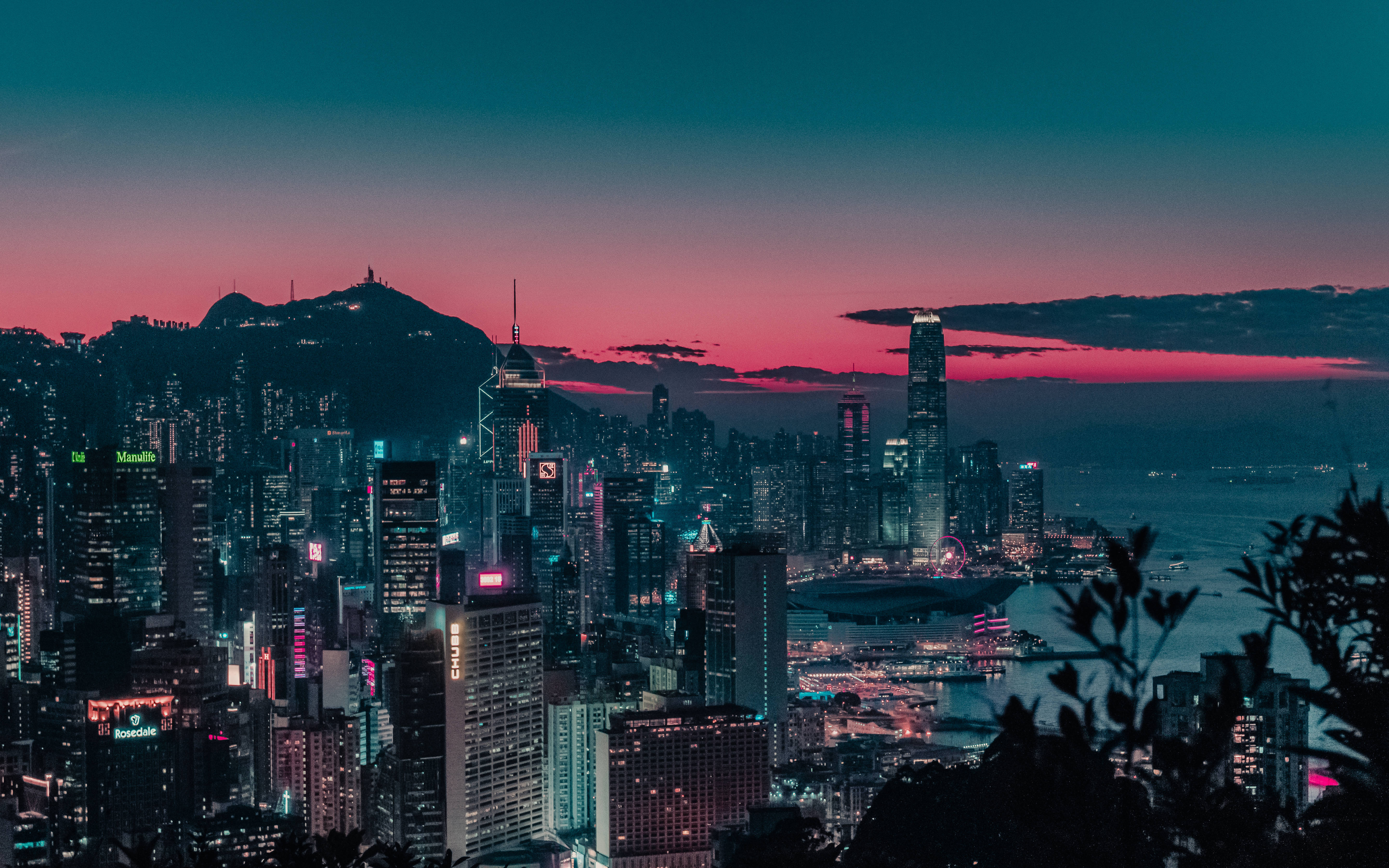 香港 桌布 壁紙 — 充滿活力的暮色城市景觀，閃爍的摩天大樓和粉紅色的天空，映襯著港口和山脈。