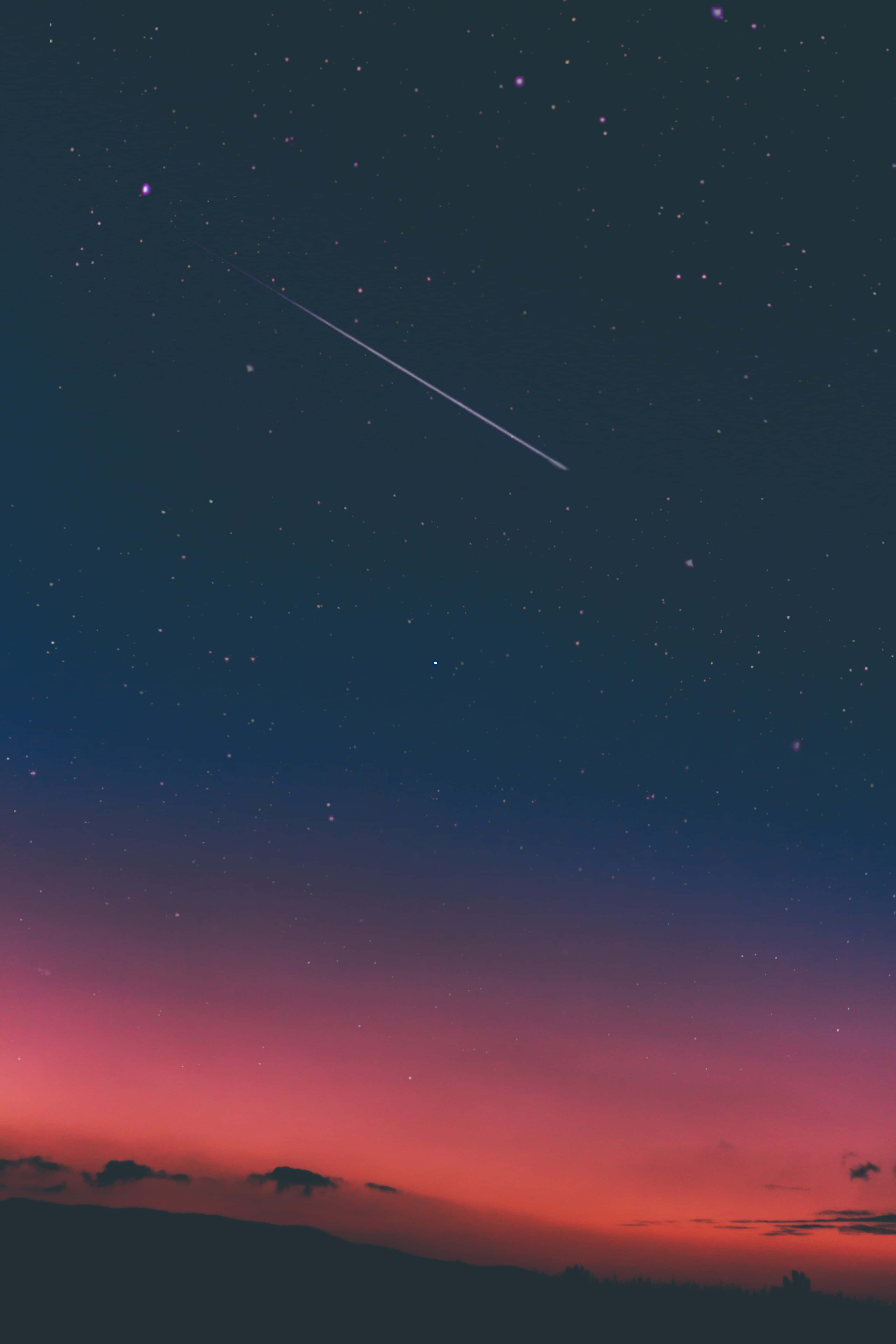 iPhone 桌布 壁紙 — 充滿活力的暮色天空，在黑暗的剪影山丘上方帶有粉紅色和橙色的條紋，被一顆明亮的流星劃破。