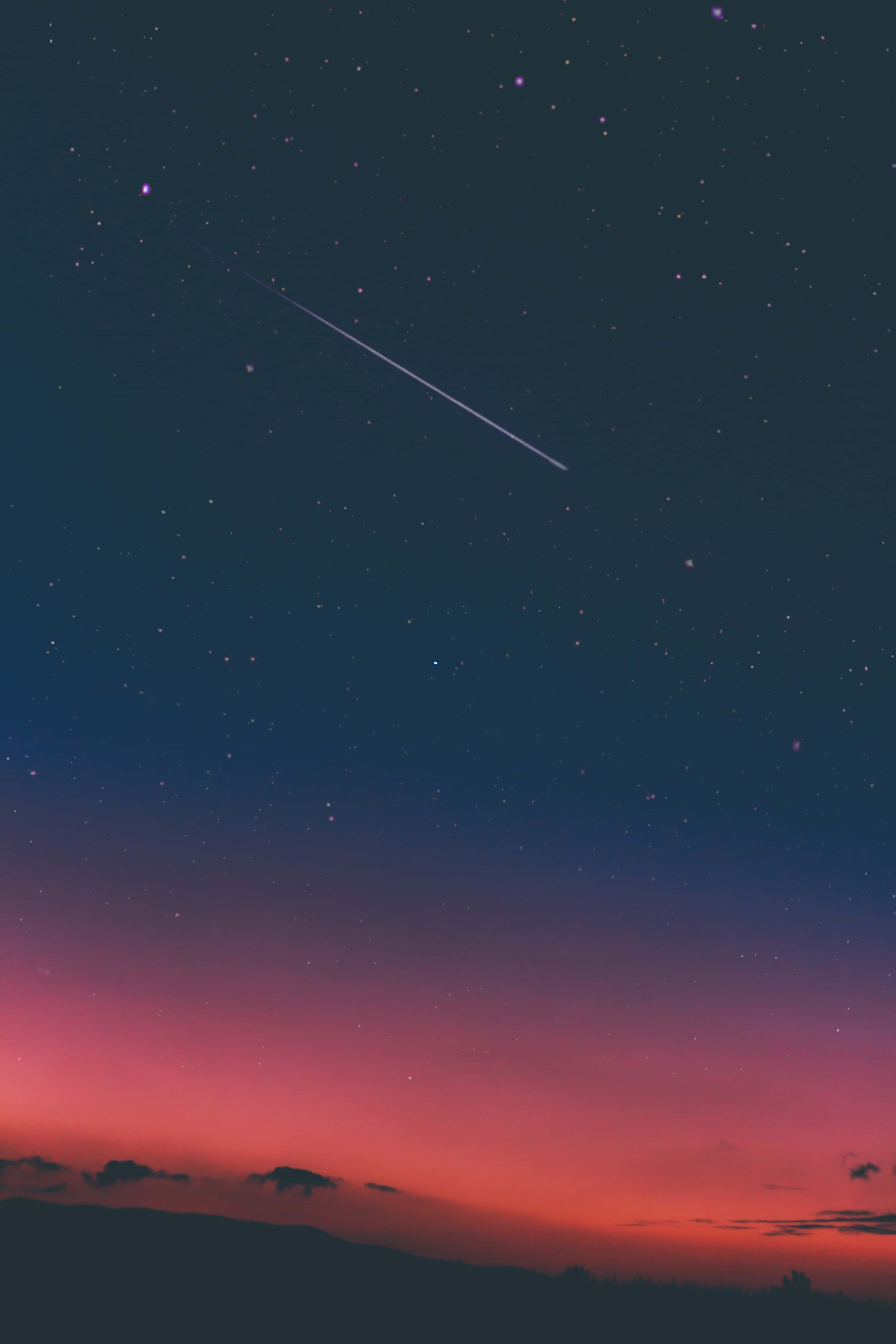 Shooting Star 桌布 壁紙 — 充滿活力的暮色天空，帶有粉紅色和紫色調，一顆明亮的流星在剪影山丘上方的星空中劃過。