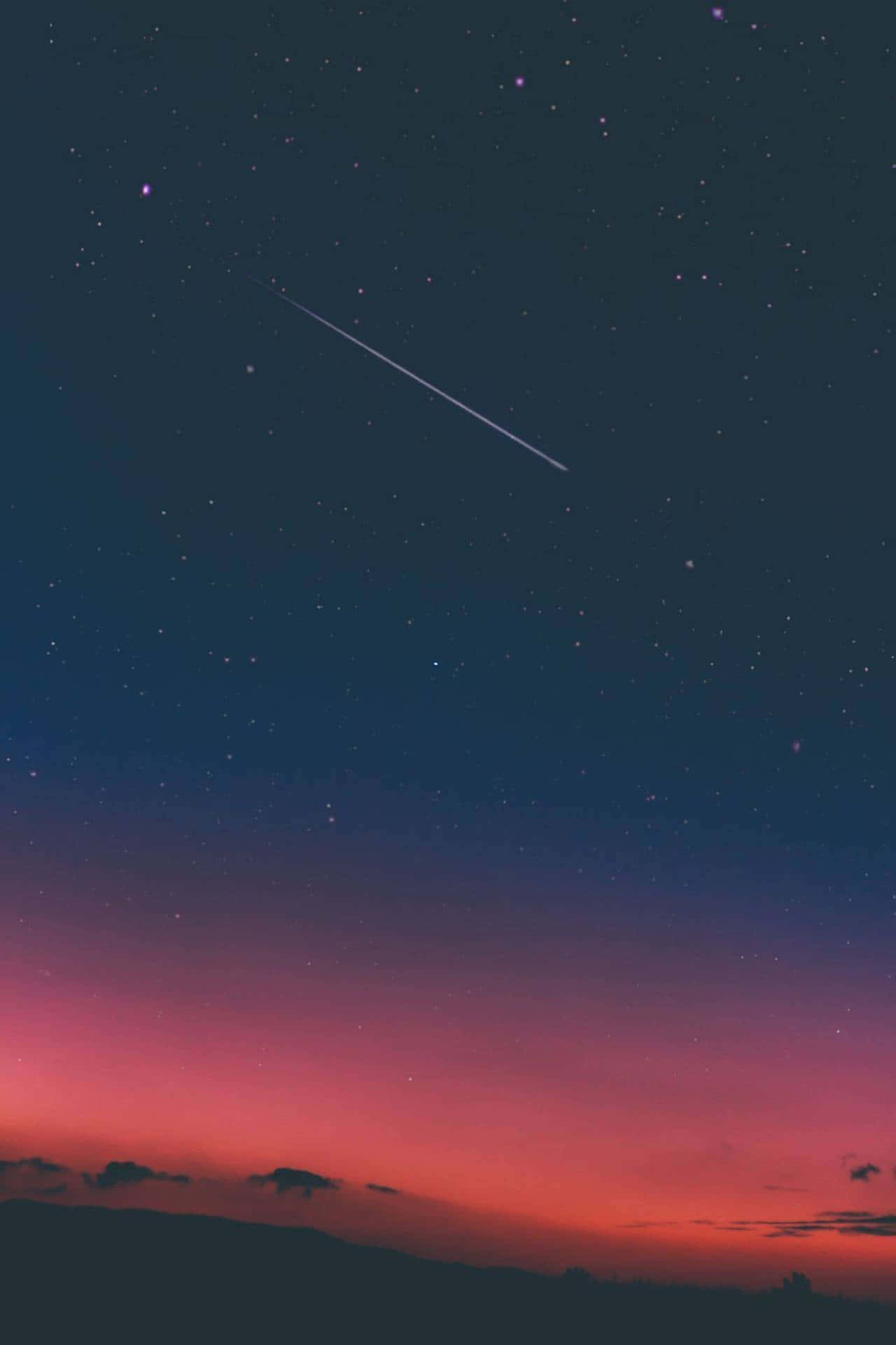 Shooting Star 桌布 壁紙 — 充滿活力的暮色天空，帶有粉紅色和紫色調，一顆明亮的流星在剪影山丘上方的星空中劃過。